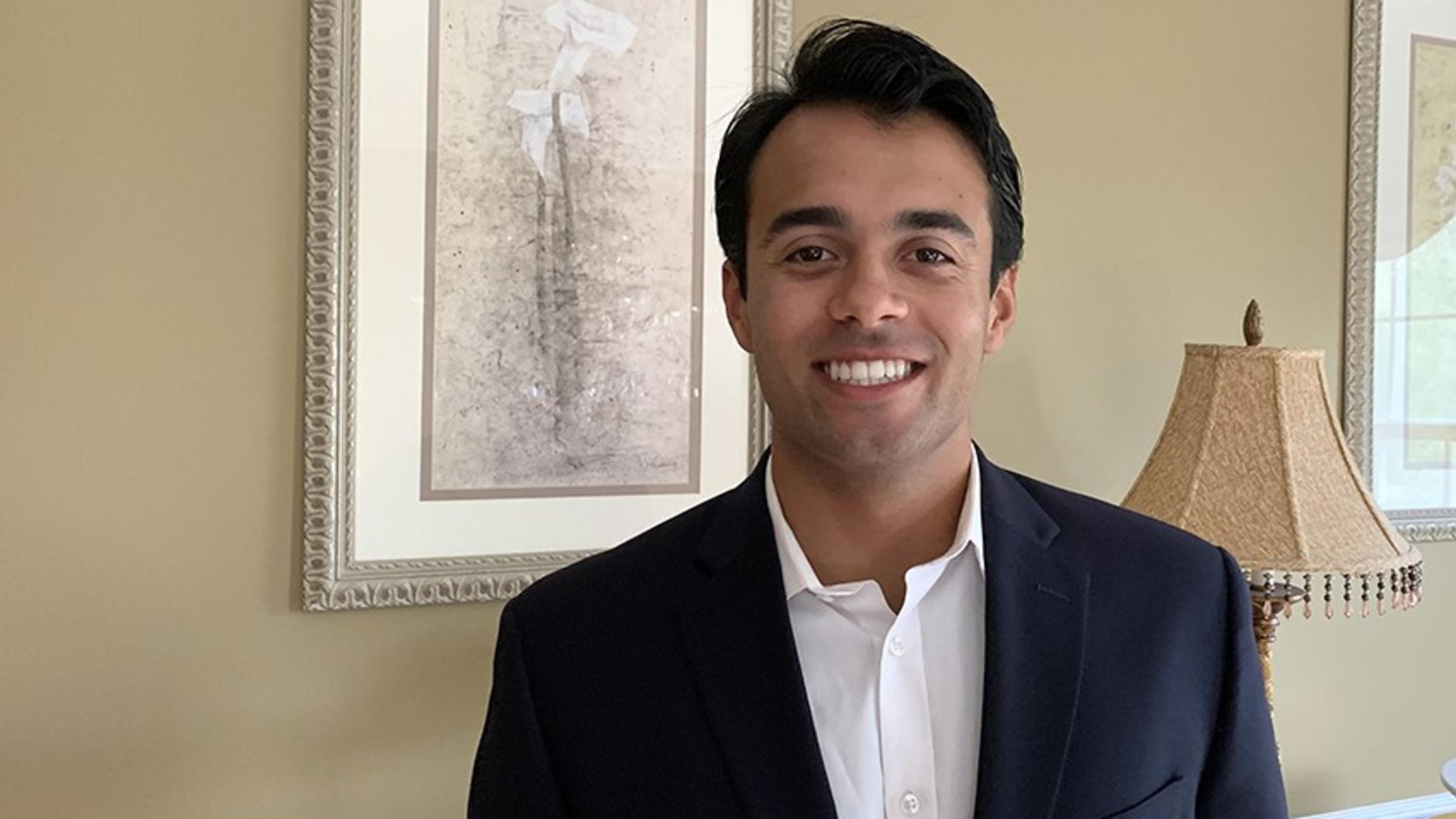 Vince Falvo poses for the camera in his home, wearing a dark jacket and white dress shirt.