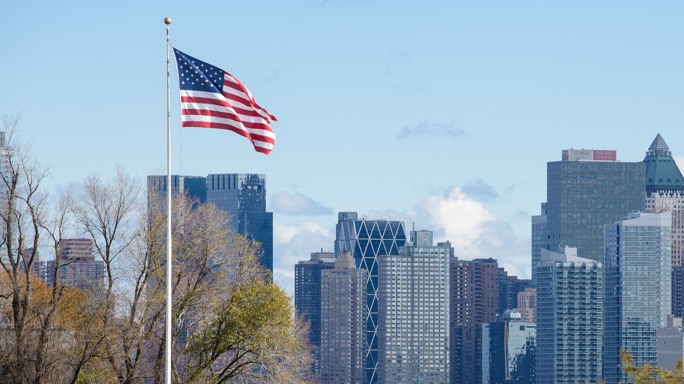 The American flag flies at full staff against a backdrop of a city