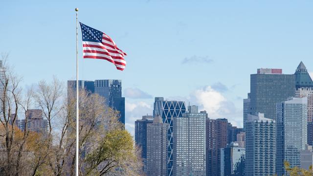 The American flag flies at full staff against a backdrop of a city