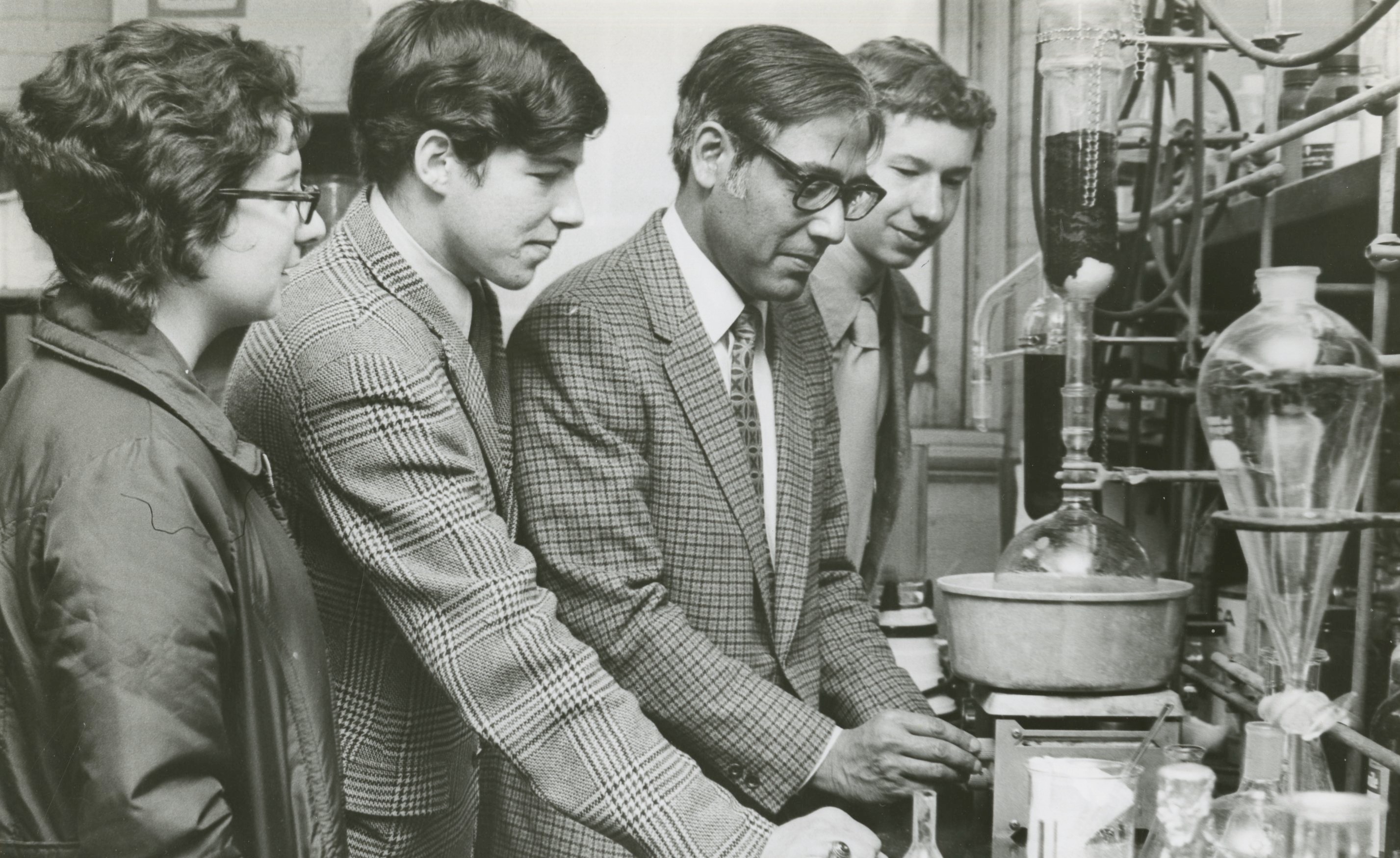 Dr. Ajay Bose works in a lab with three students in a vintage photo.