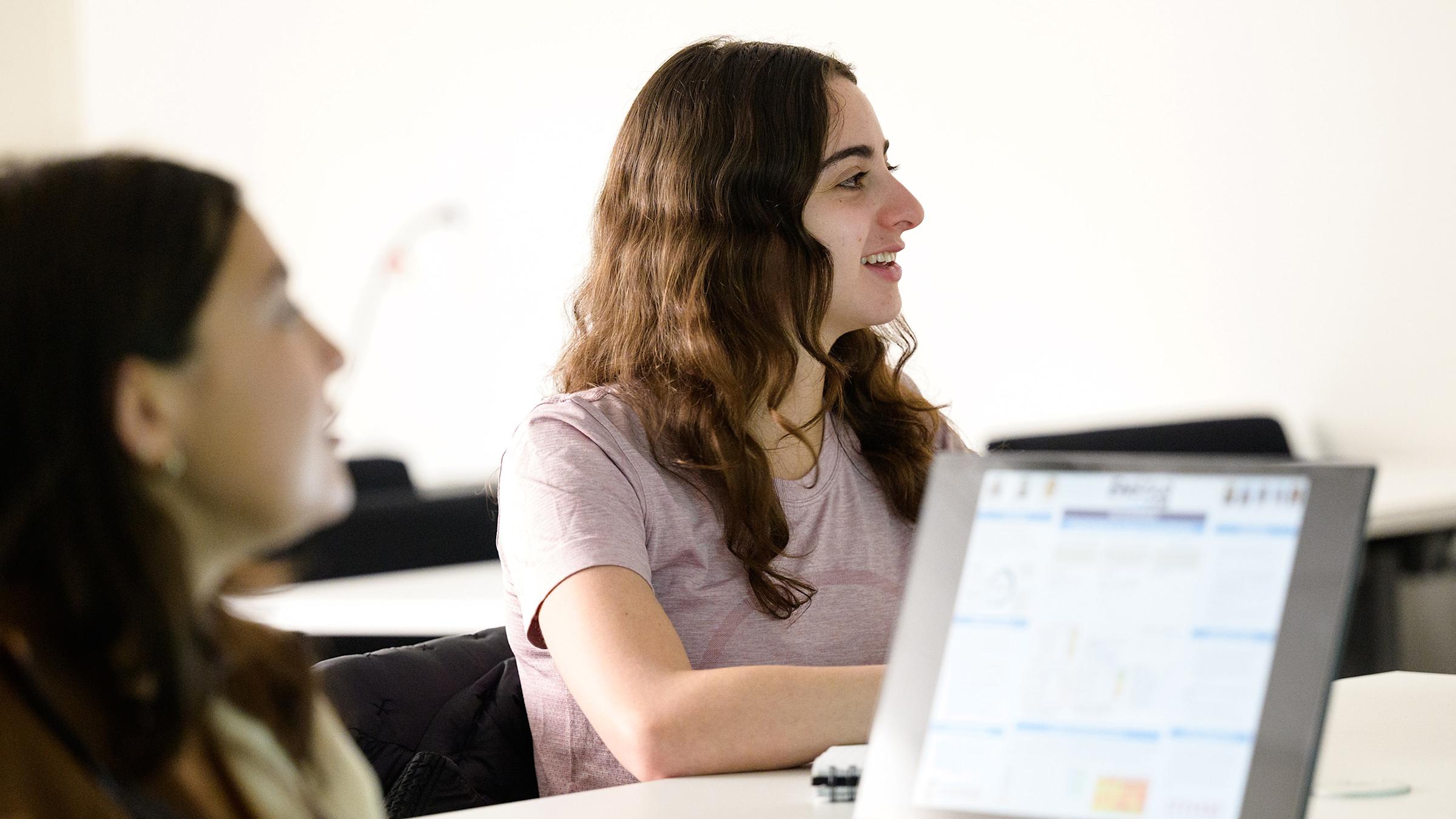 Two undergraduate students listening to a lecture and working on a laptop