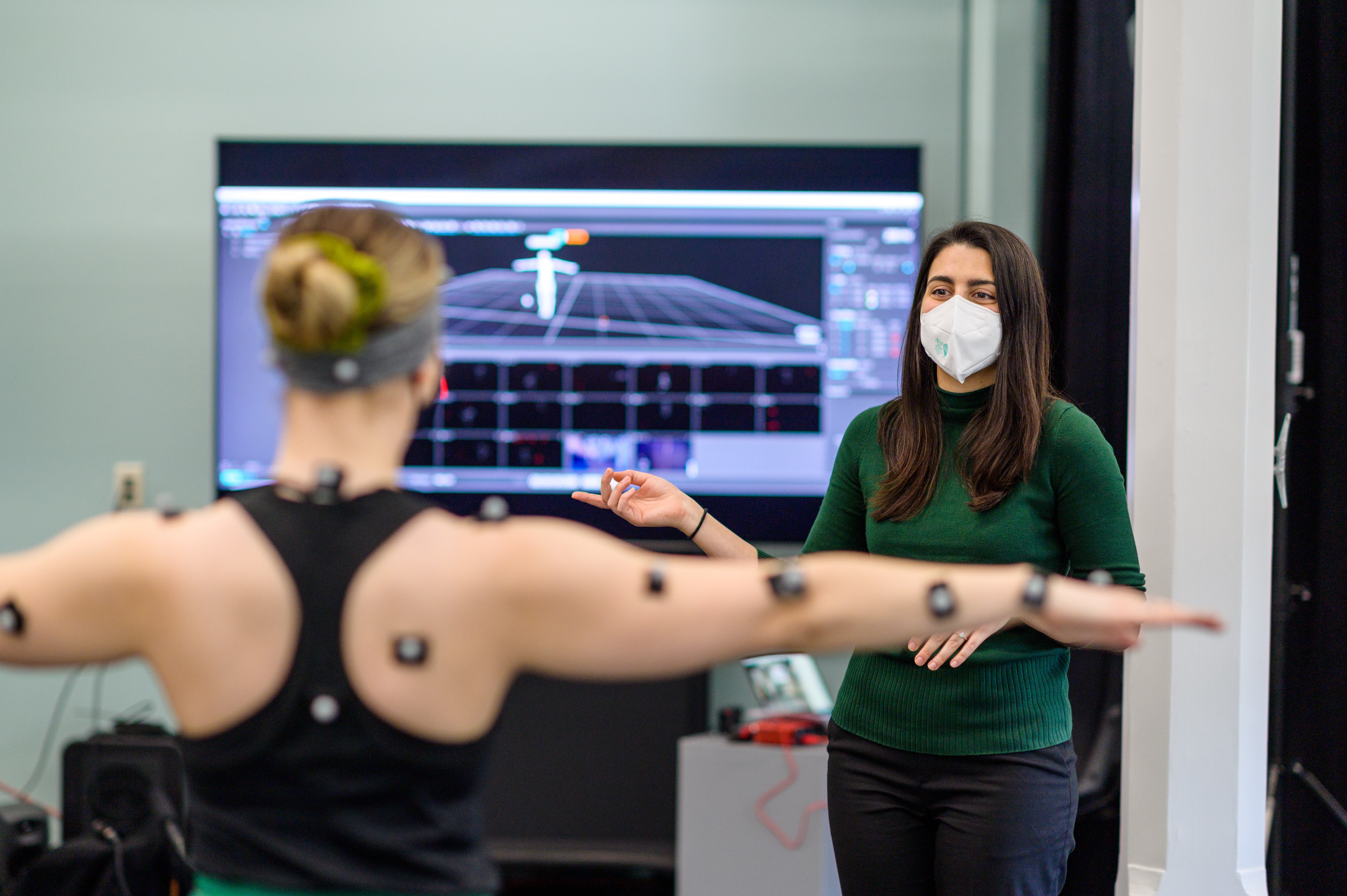 Model with motion capture nodes attached to arms raises arms with instructor in background