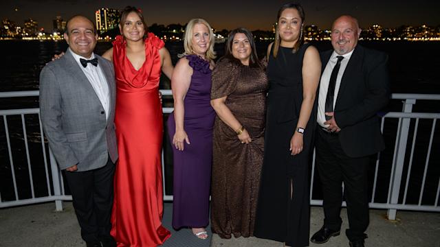 Members of the Stevens community gather for a picture on the water at the Stevens Awards Gala, with the Stevens campus in the background
