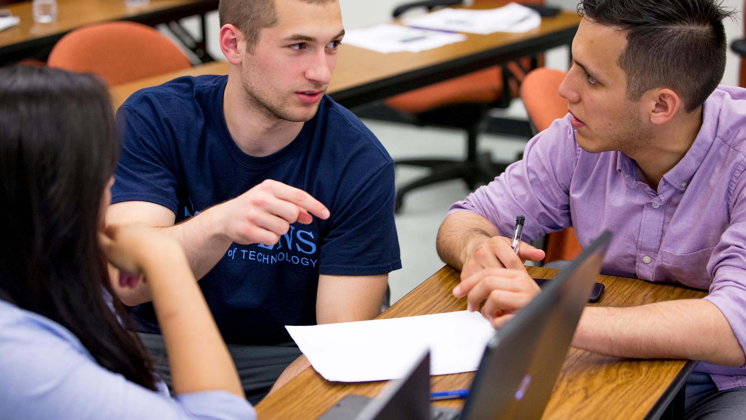Three graduate systems engineering students work together at a table during class.