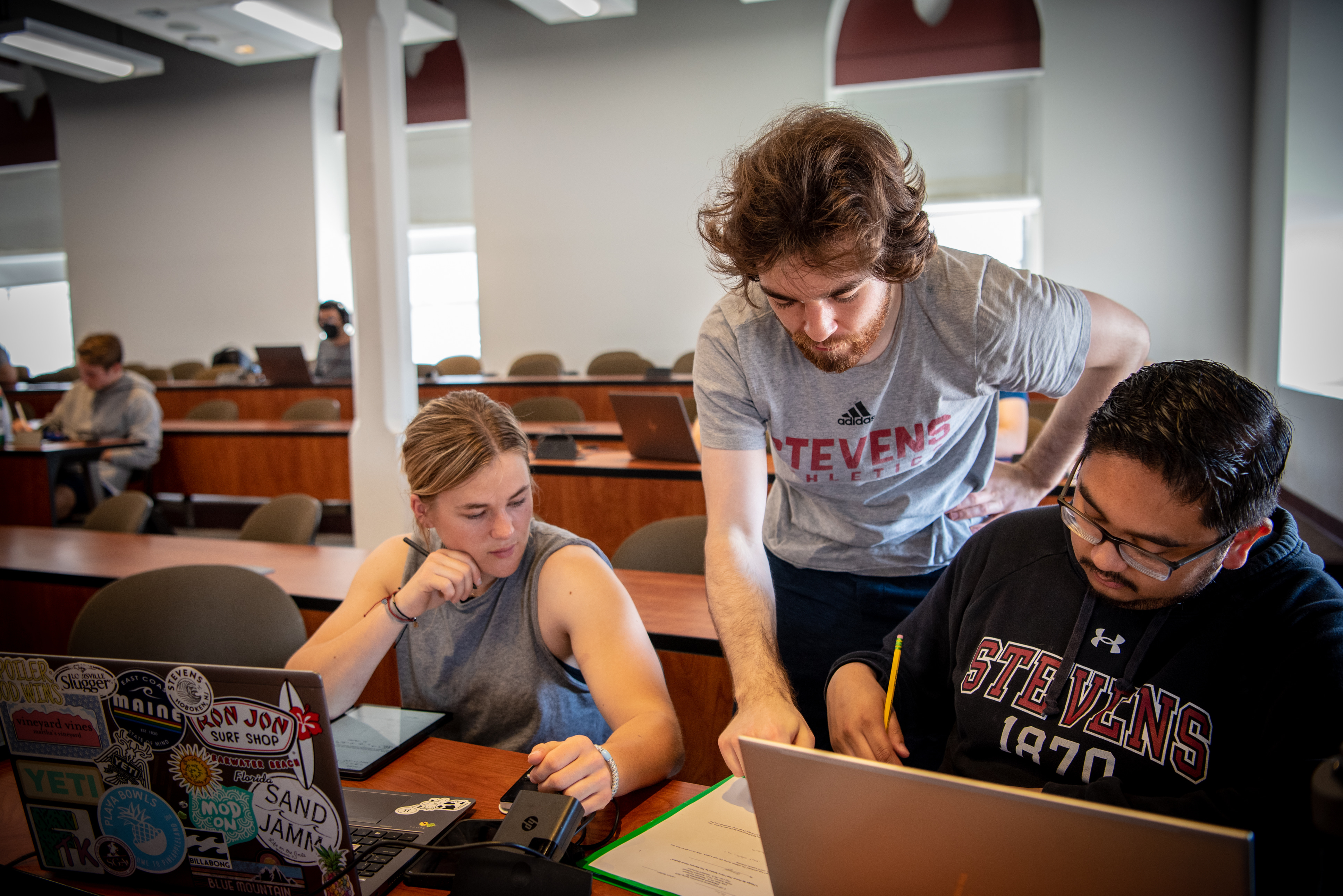 Three Engineering Management students looking at a laptop in class.