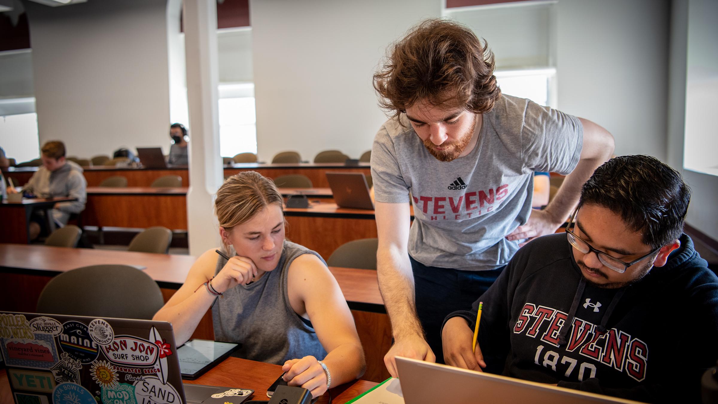 Three Engineering Management students looking at a laptop in class.