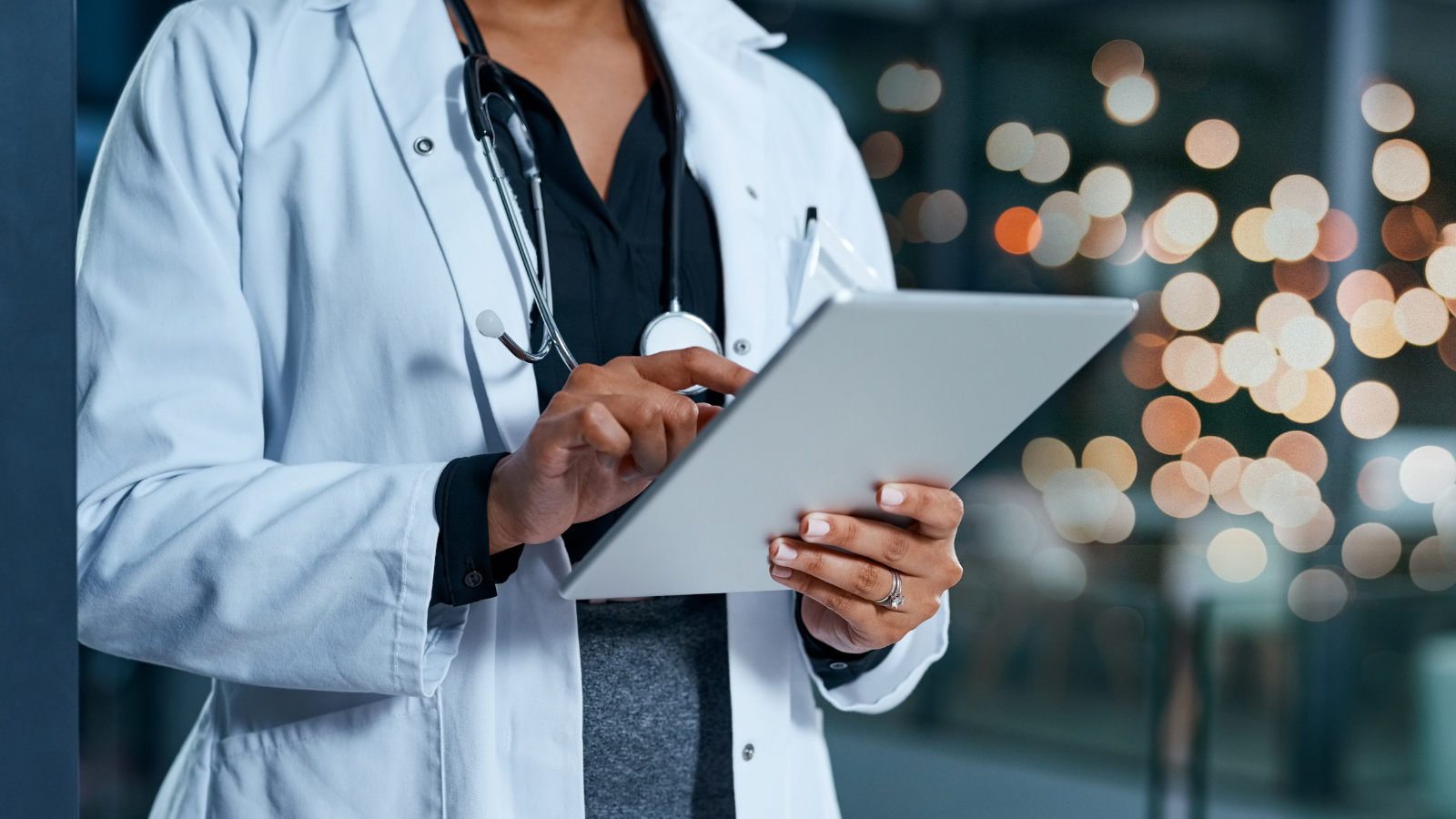 A person in a doctor's lab coat holding and operating a tablet.