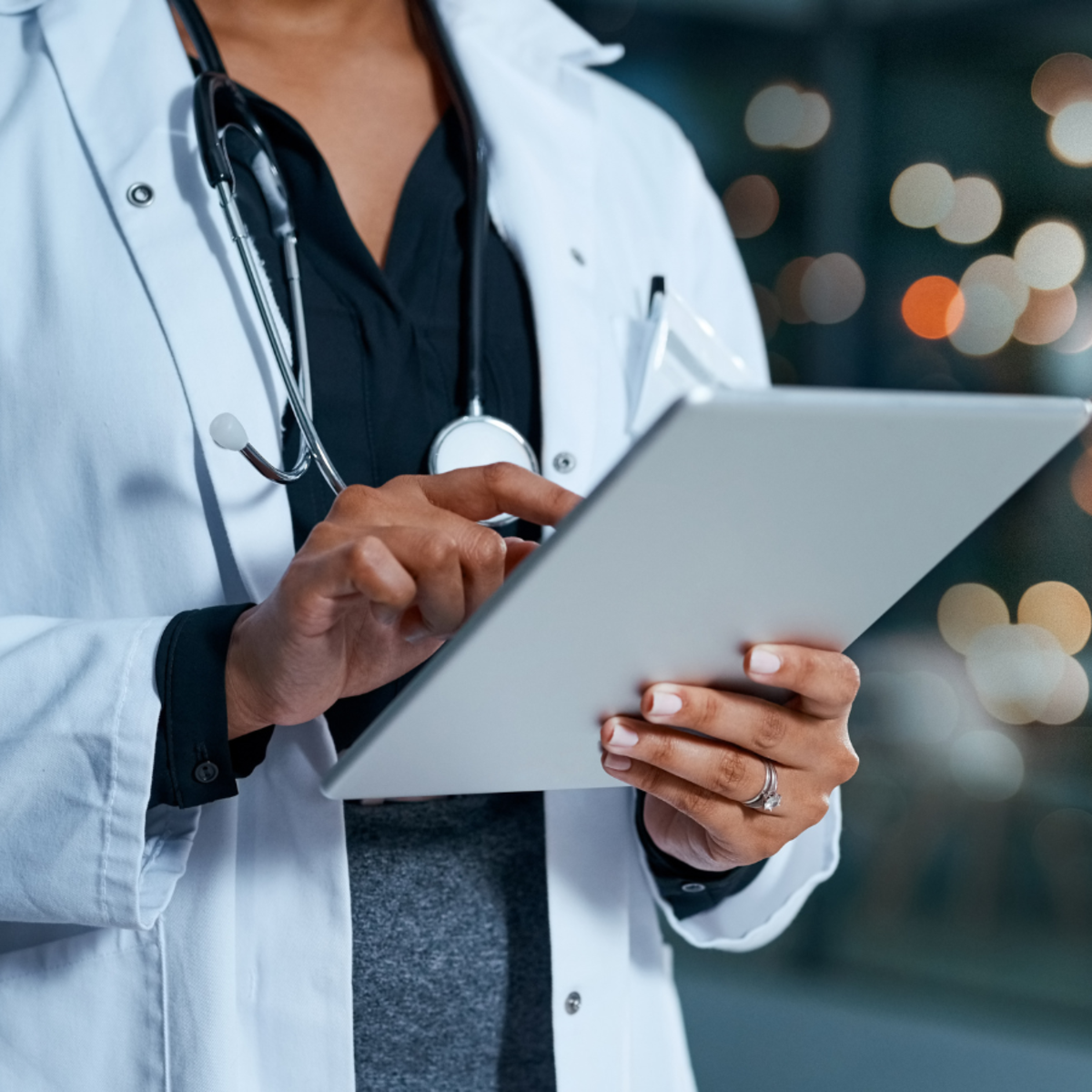 A person in a doctor's lab coat holding and operating a tablet.