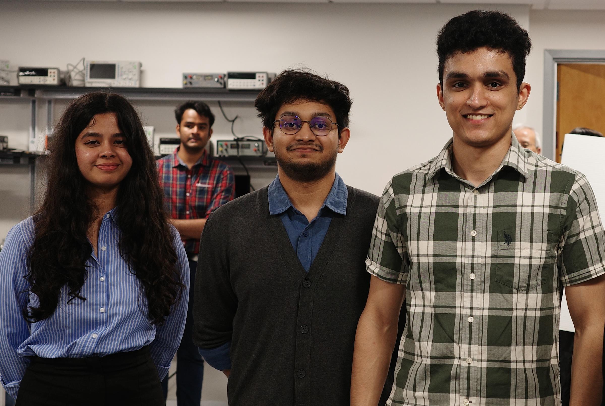 Three students stand in a lab together, smiling at the camera