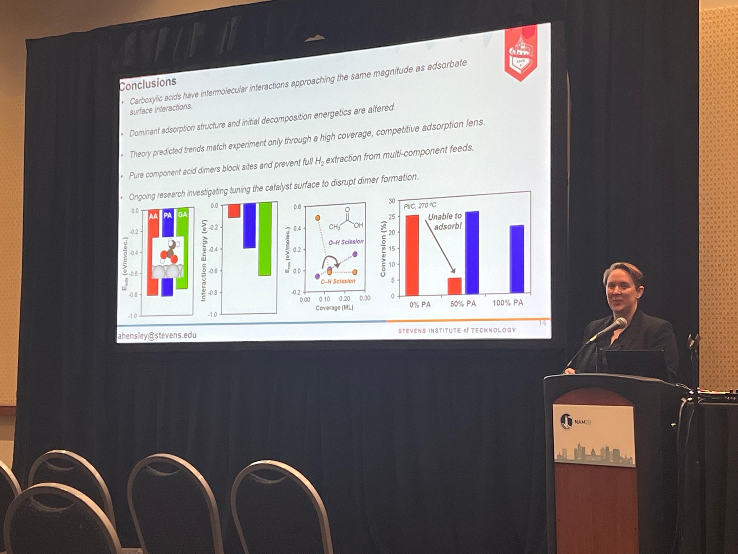 Alyssa Hensley stands at a podium with scientific research portrayed on a large projector behind her