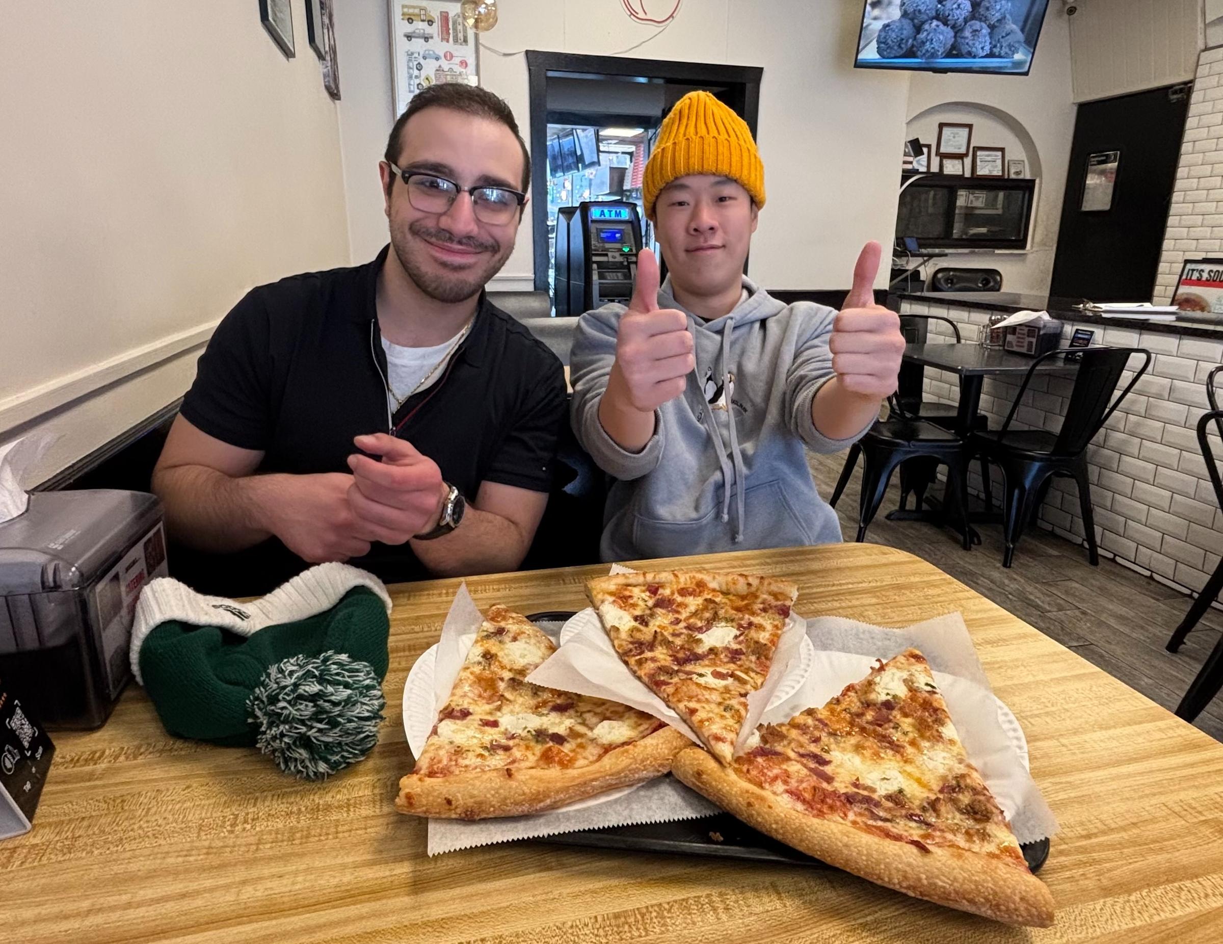 Student researchers Michael Lazieh and Daniel Fong sit in a restaurant with three slices of pizza.