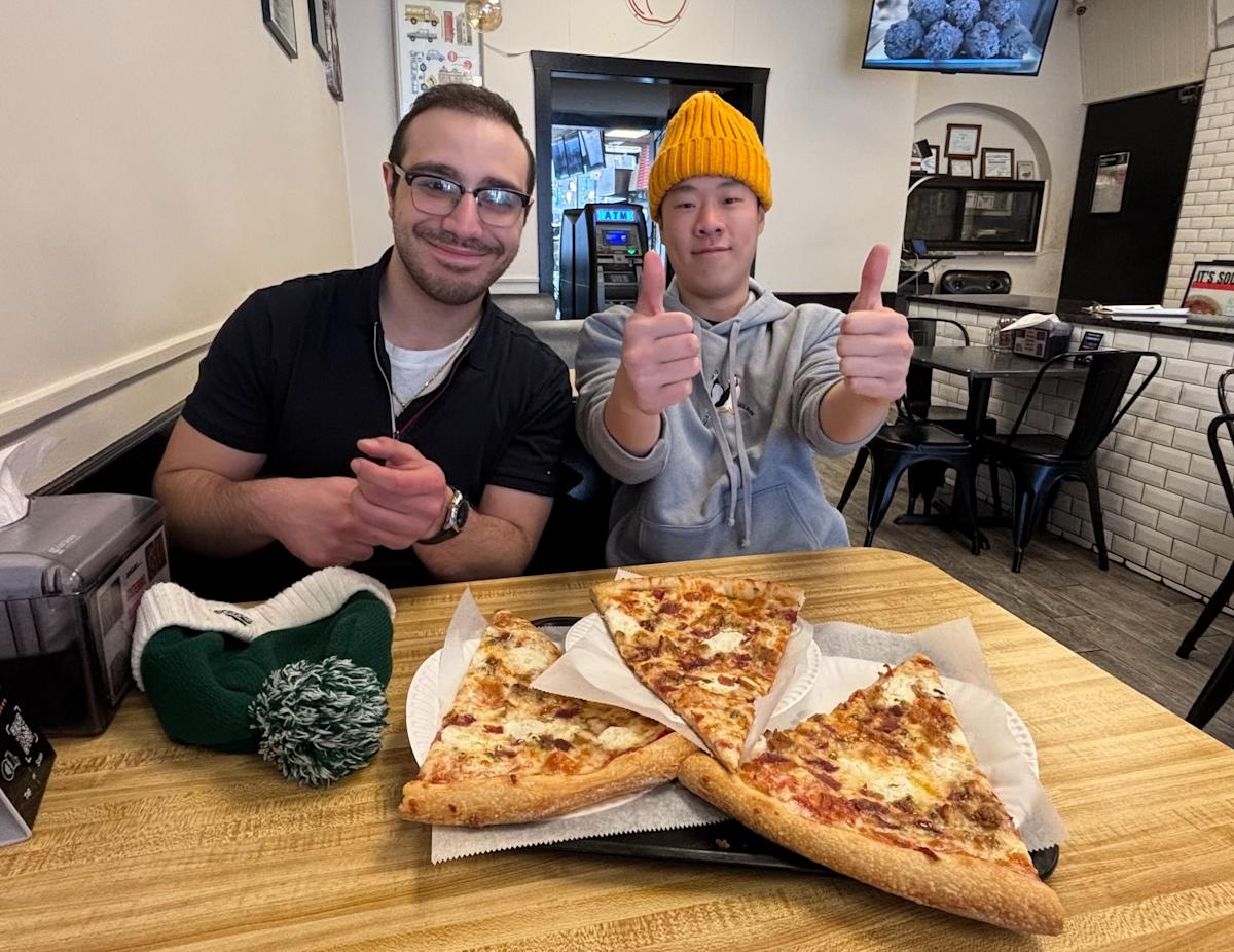 Student researchers Michael Lazieh and Daniel Fong sit in a restaurant with three slices of pizza.