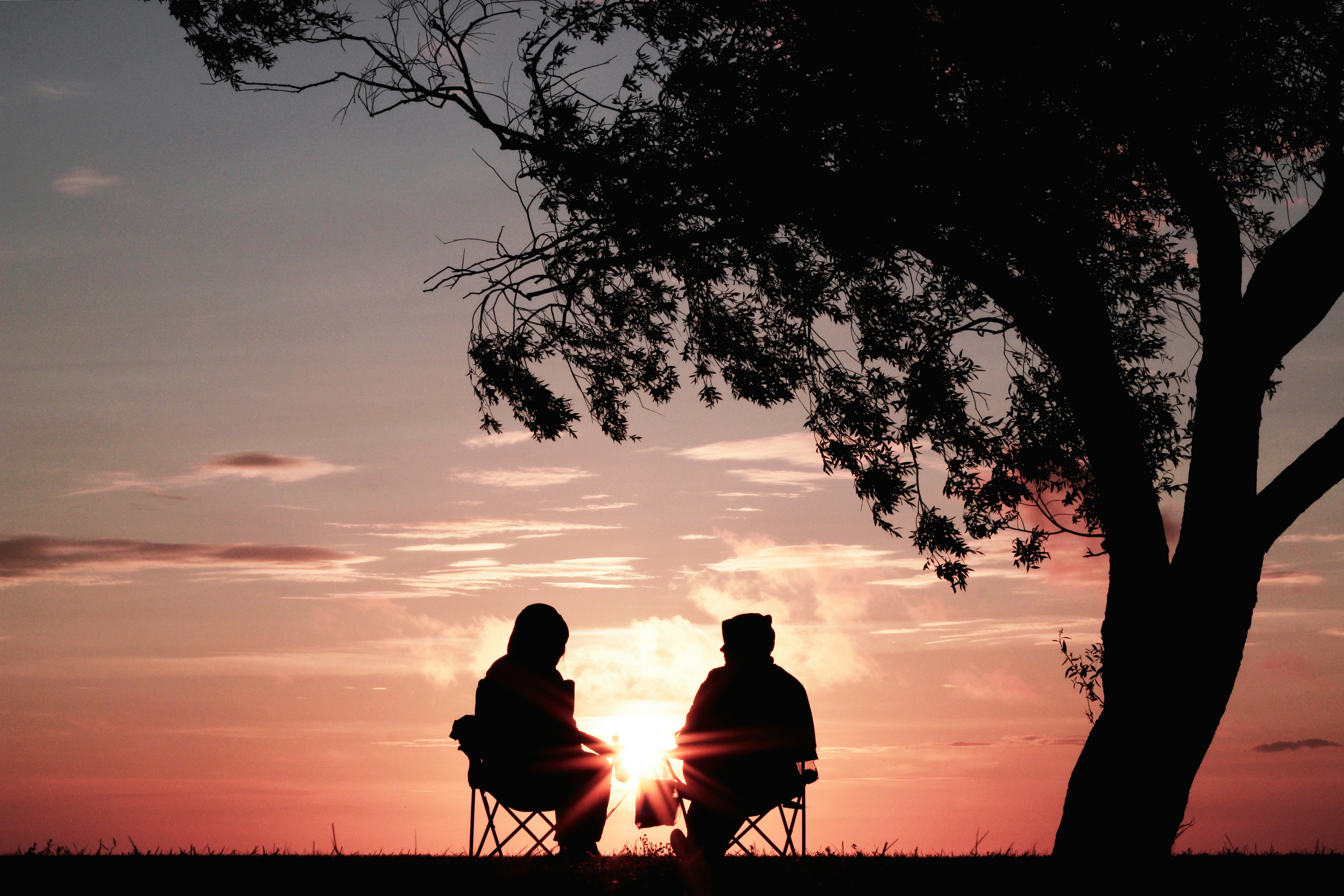 Two elderly people sitting in silhouette against sunset