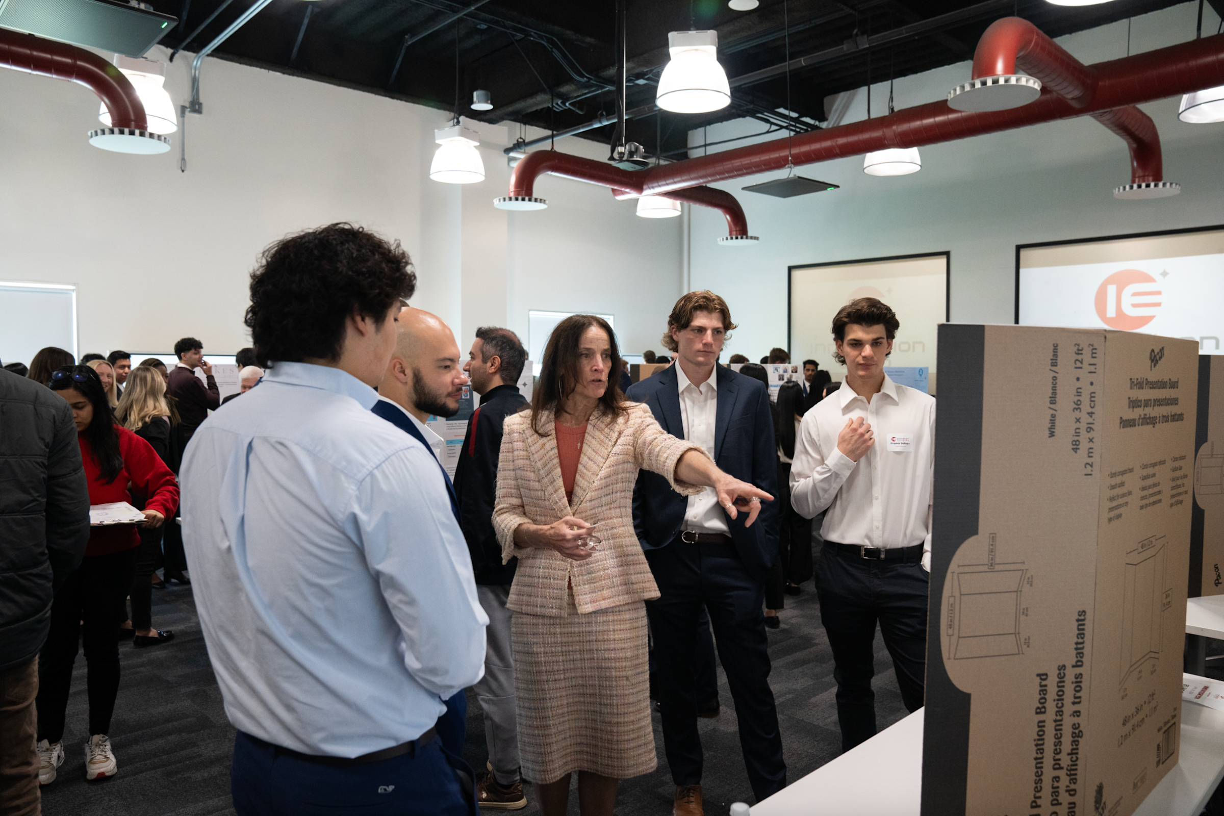 A faculty advisor talks with a group of students, pointing at the posterboard. 