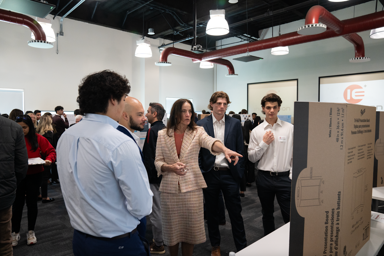 A faculty advisor talks with a group of students, pointing at the posterboard. 