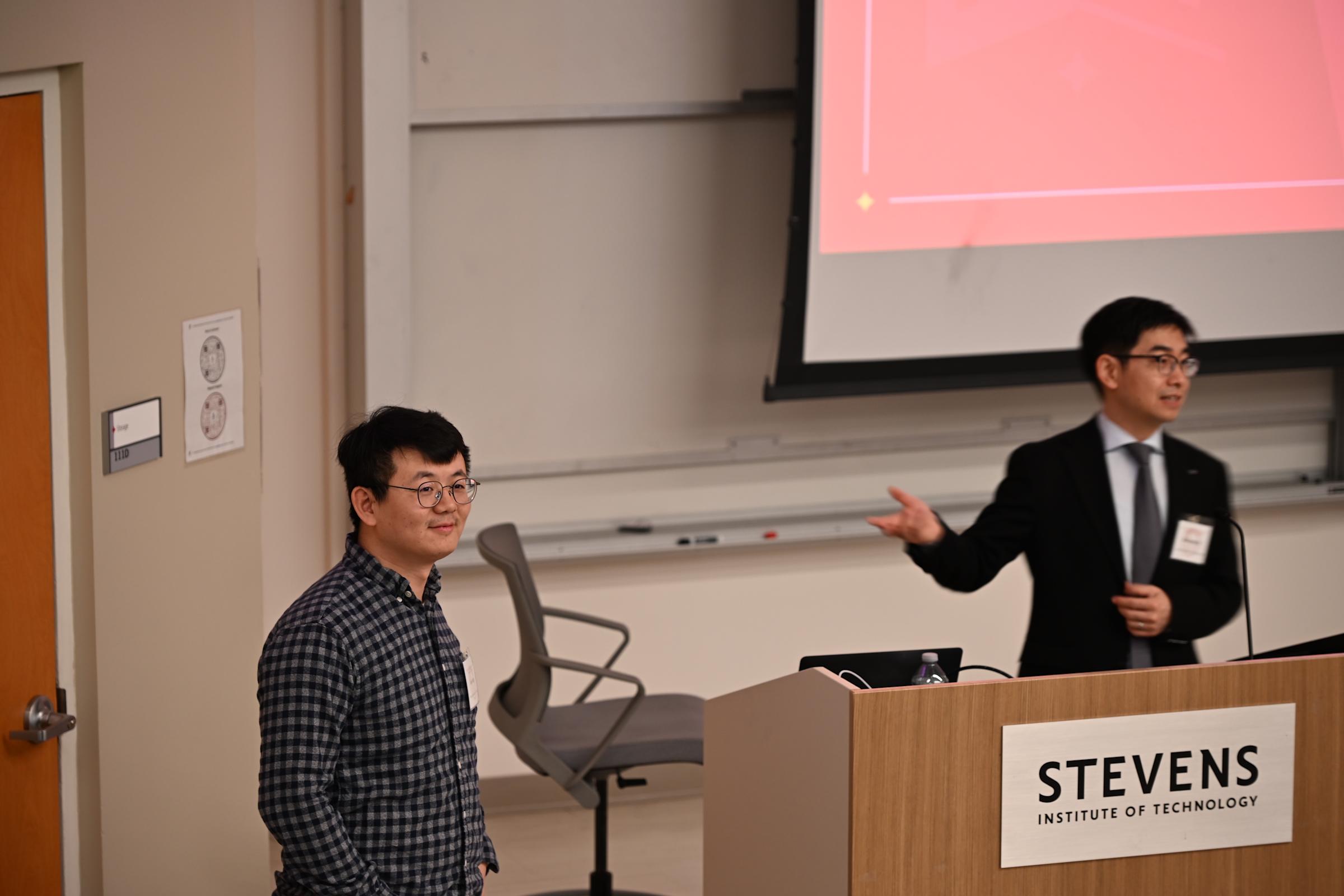 A photo of a person in a suit behind a podium introducing another person to his right.