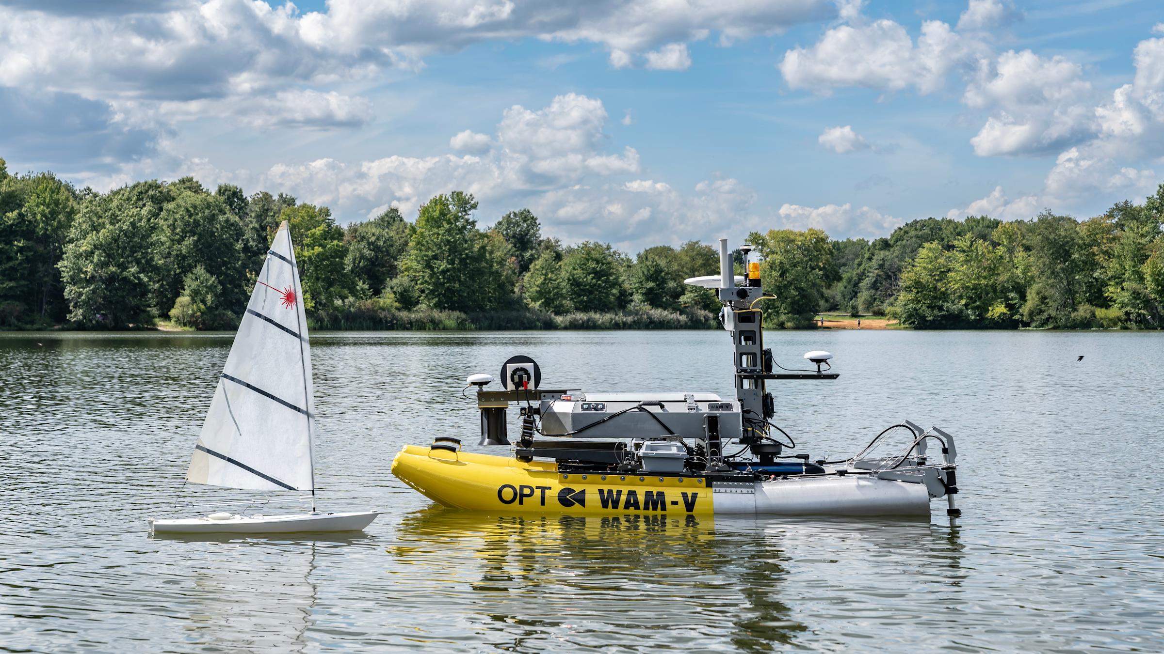 A photograph of the WAM-V 8 and a sailboat sitting on the water.