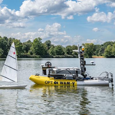 A photograph of the WAM-V 8 and a sailboat sitting on the water.