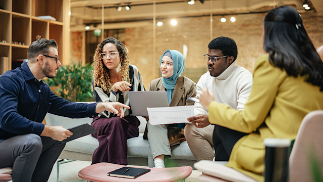 Group of diverse workers sit together discussing ideas