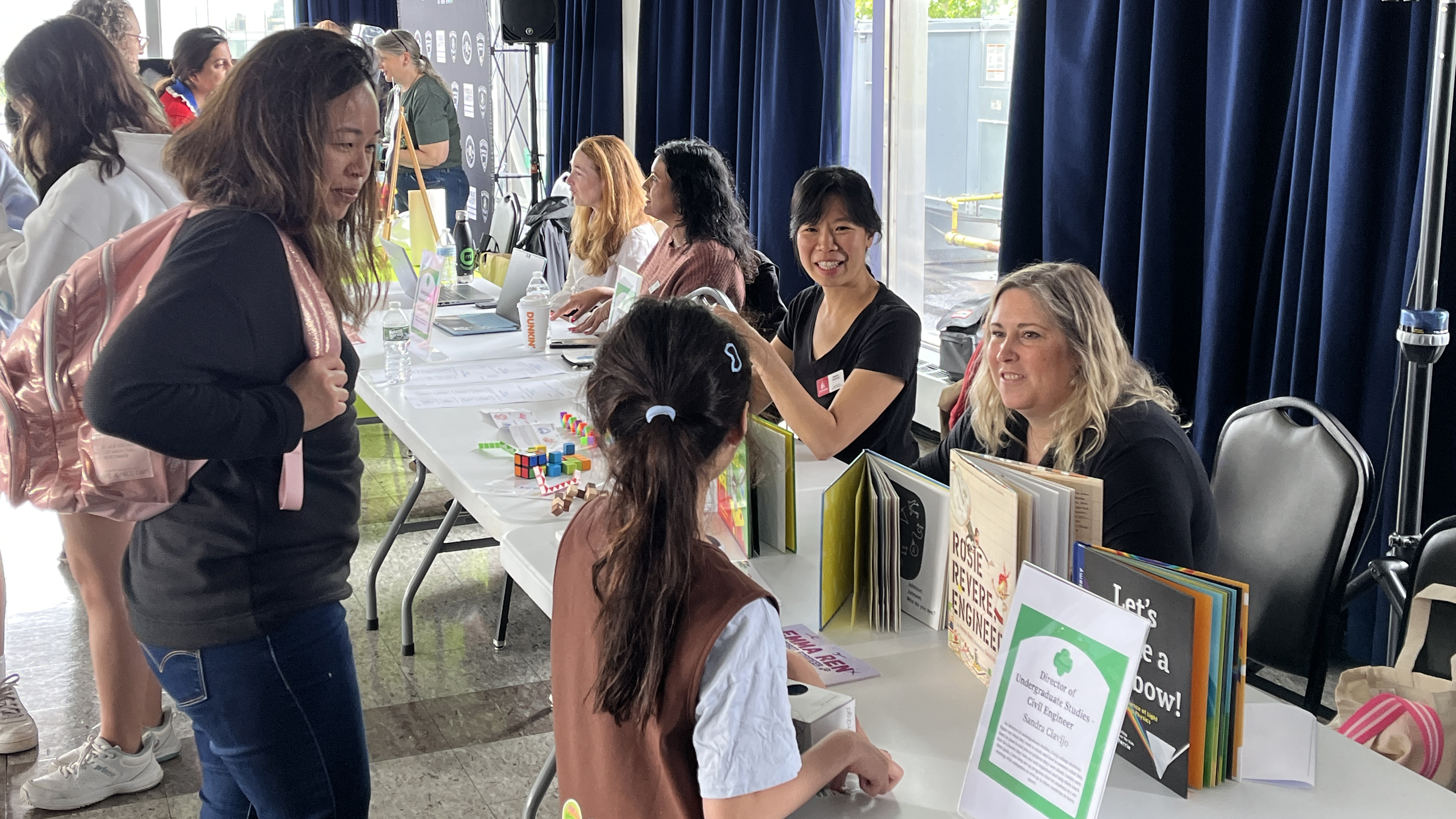 A Girl Scout and an adult speak to Stevens representatives at a table lined with books.