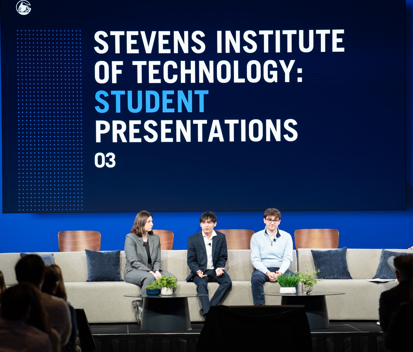 Four people sit on stage in front of a sign that says "Stevens Institute of Technology: Student Presentations."