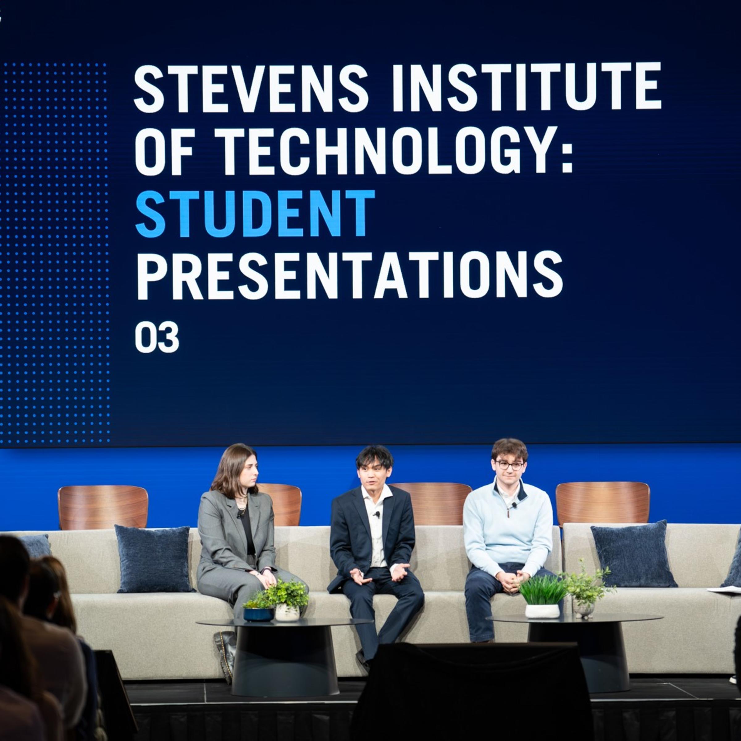 Four people sit on stage in front of a sign that says "Stevens Institute of Technology: Student Presentations."