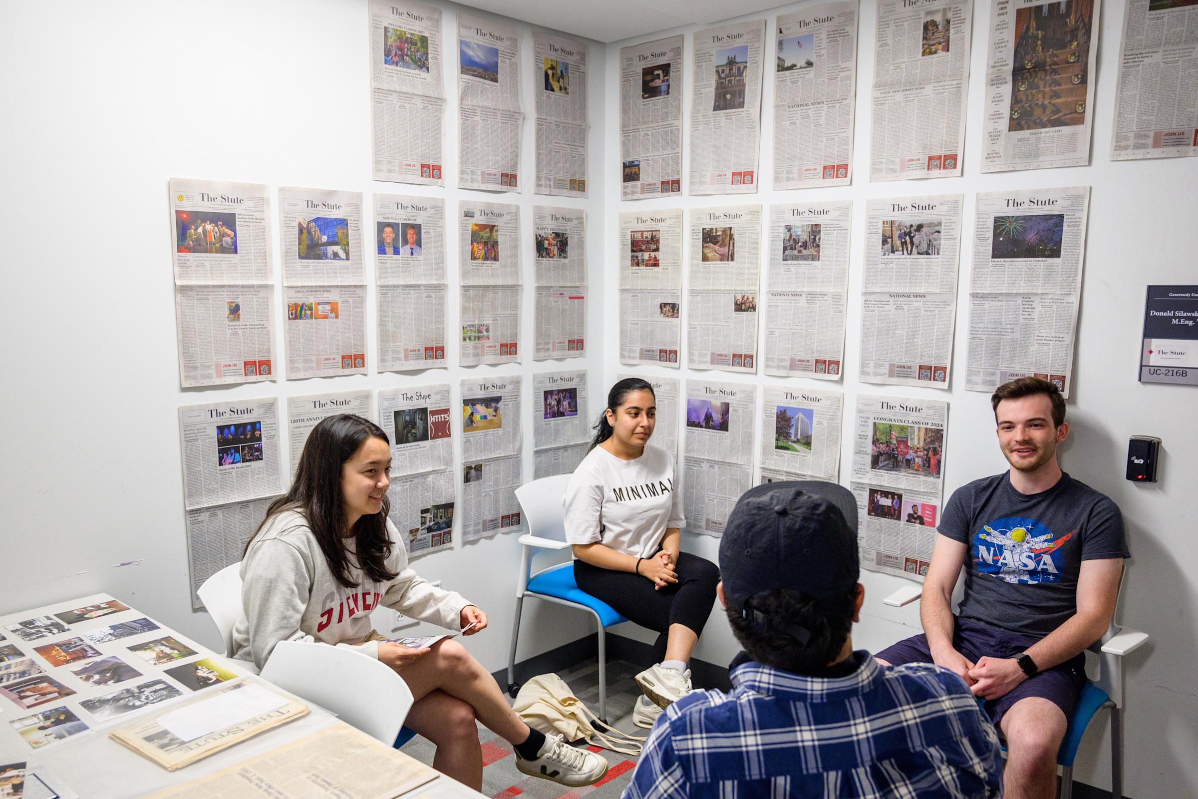 Four Stute editors gather underneath a displayed collection of Stute cover pages.