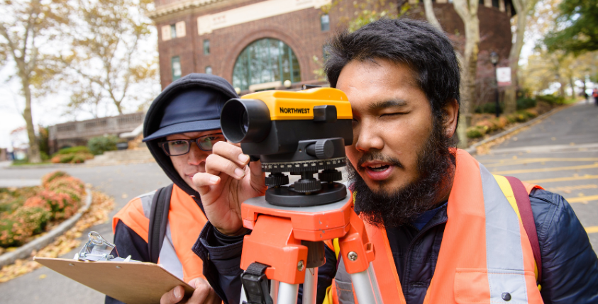 Two civil engineering students use a surveying tool on the Stevens campus.