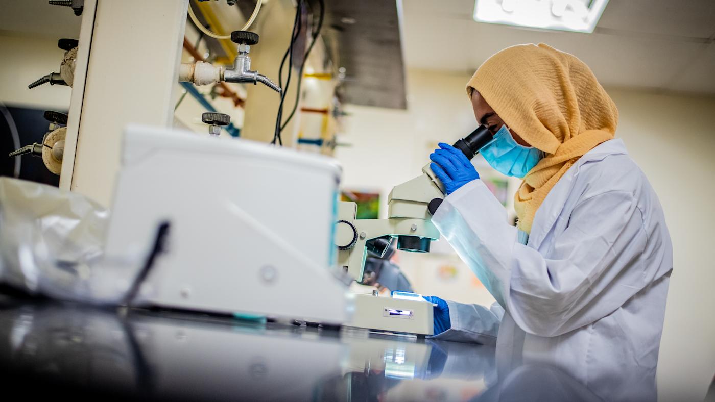 Student in lab looks into microscope.