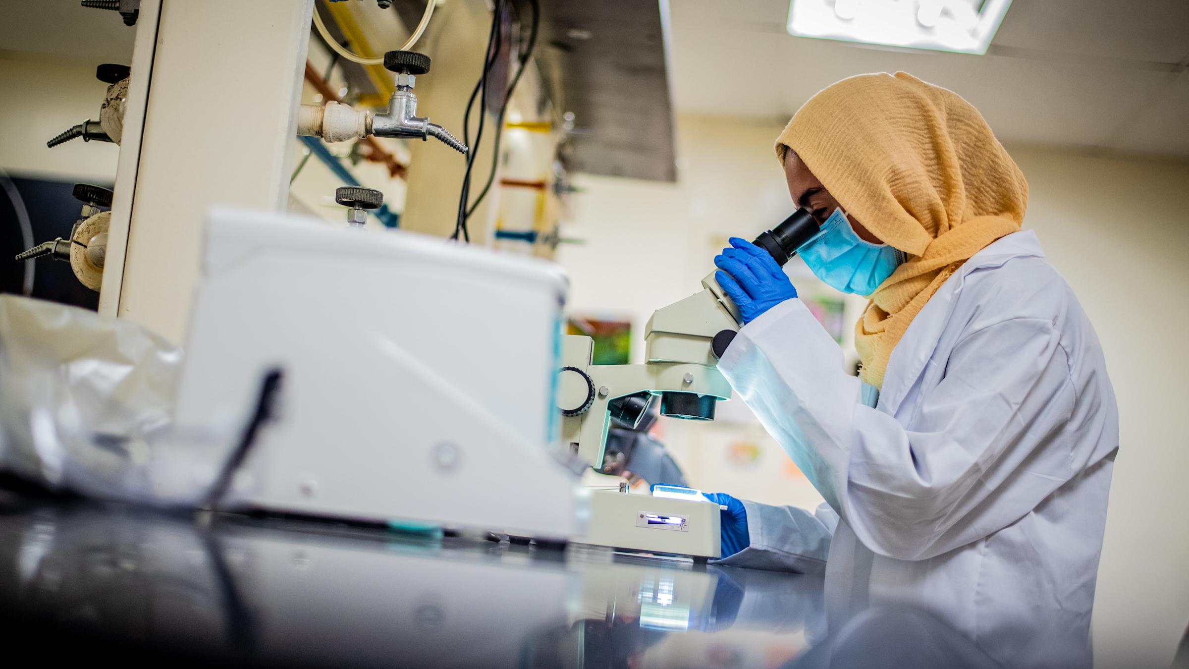 Student in lab looks into microscope.
