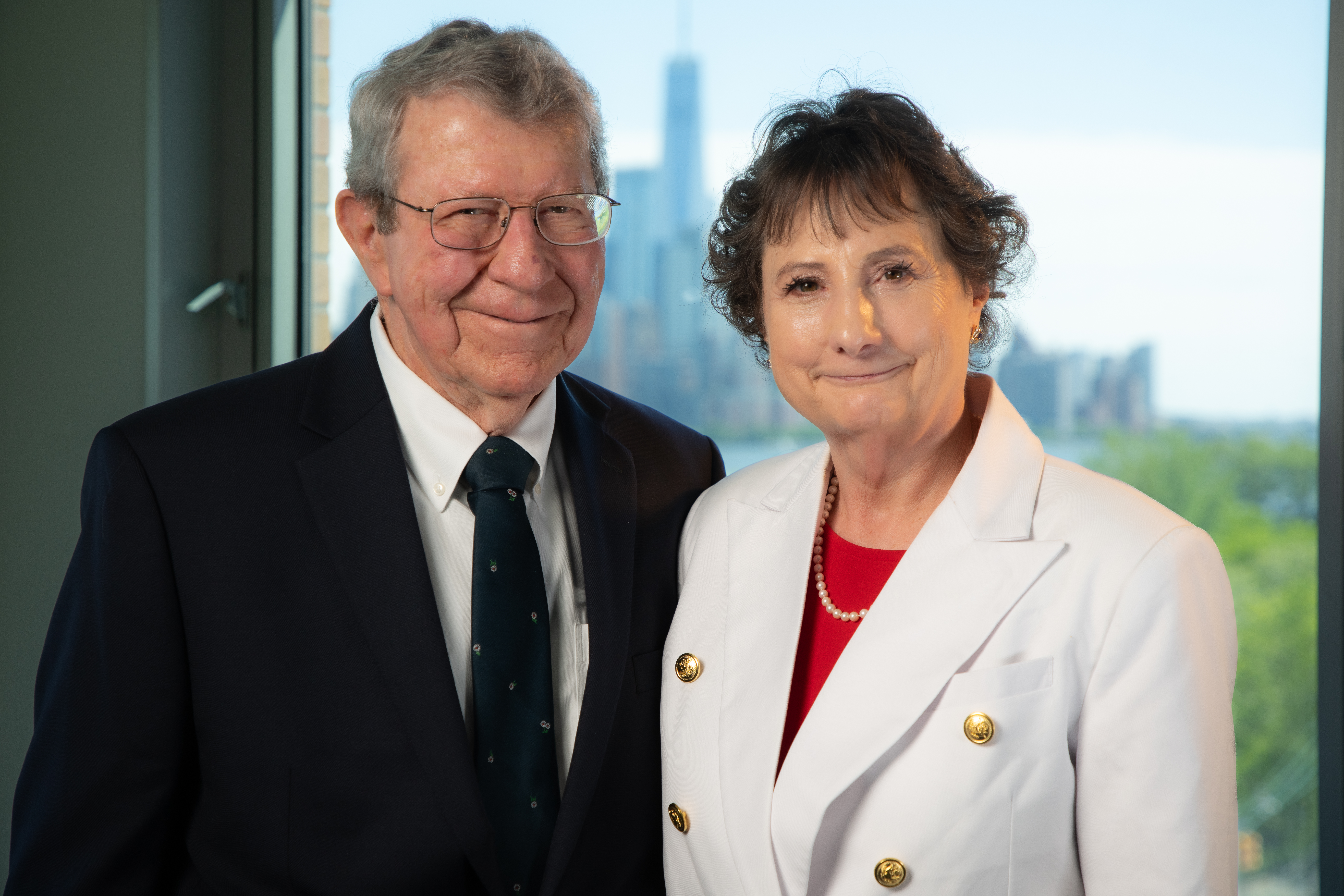 Mary VanLeer M.Eng. ’12 and her husband Will in business attire in front of a window at Stevens Institute of Technology overlooking the NYC skyline