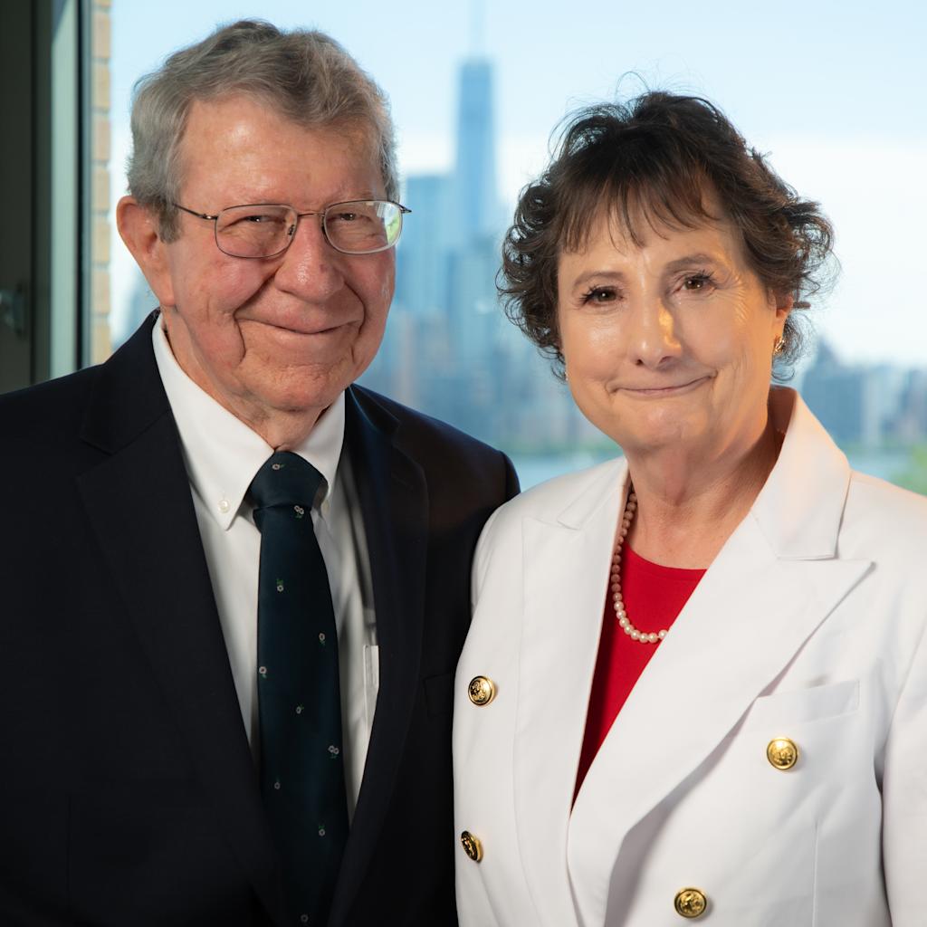 Mary VanLeer M.Eng. ’12 and her husband Will in business attire in front of a window at Stevens Institute of Technology overlooking the NYC skyline