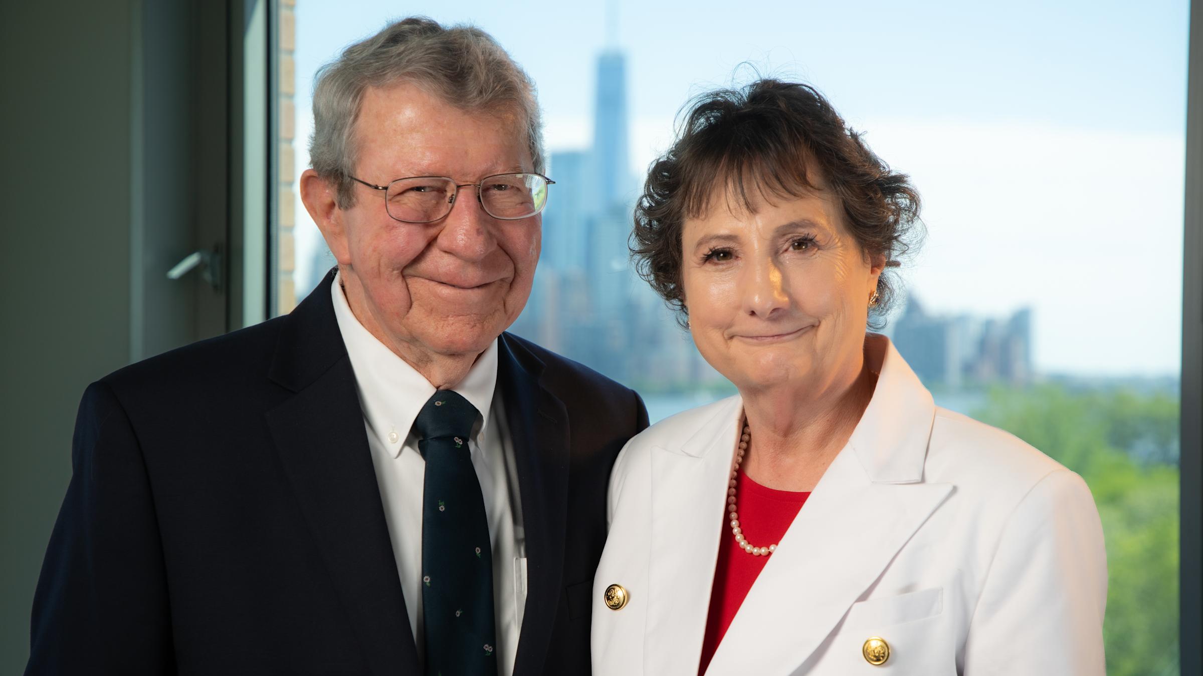 Mary VanLeer M.Eng. ’12 and her husband Will in business attire in front of a window at Stevens Institute of Technology overlooking the NYC skyline