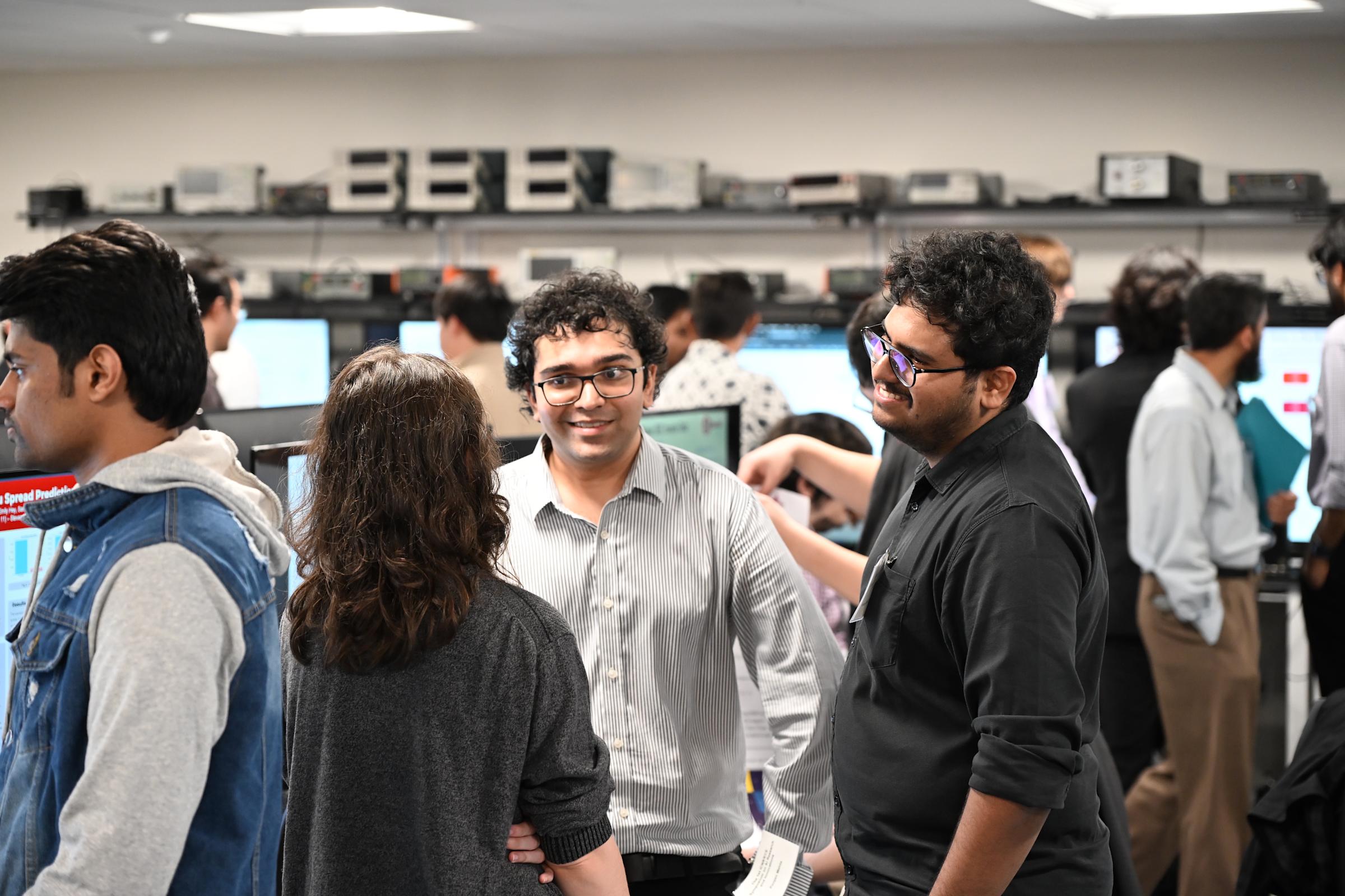 A crowd of students, with four people in the foreground and more in the background, walk around talking and looking at posters.