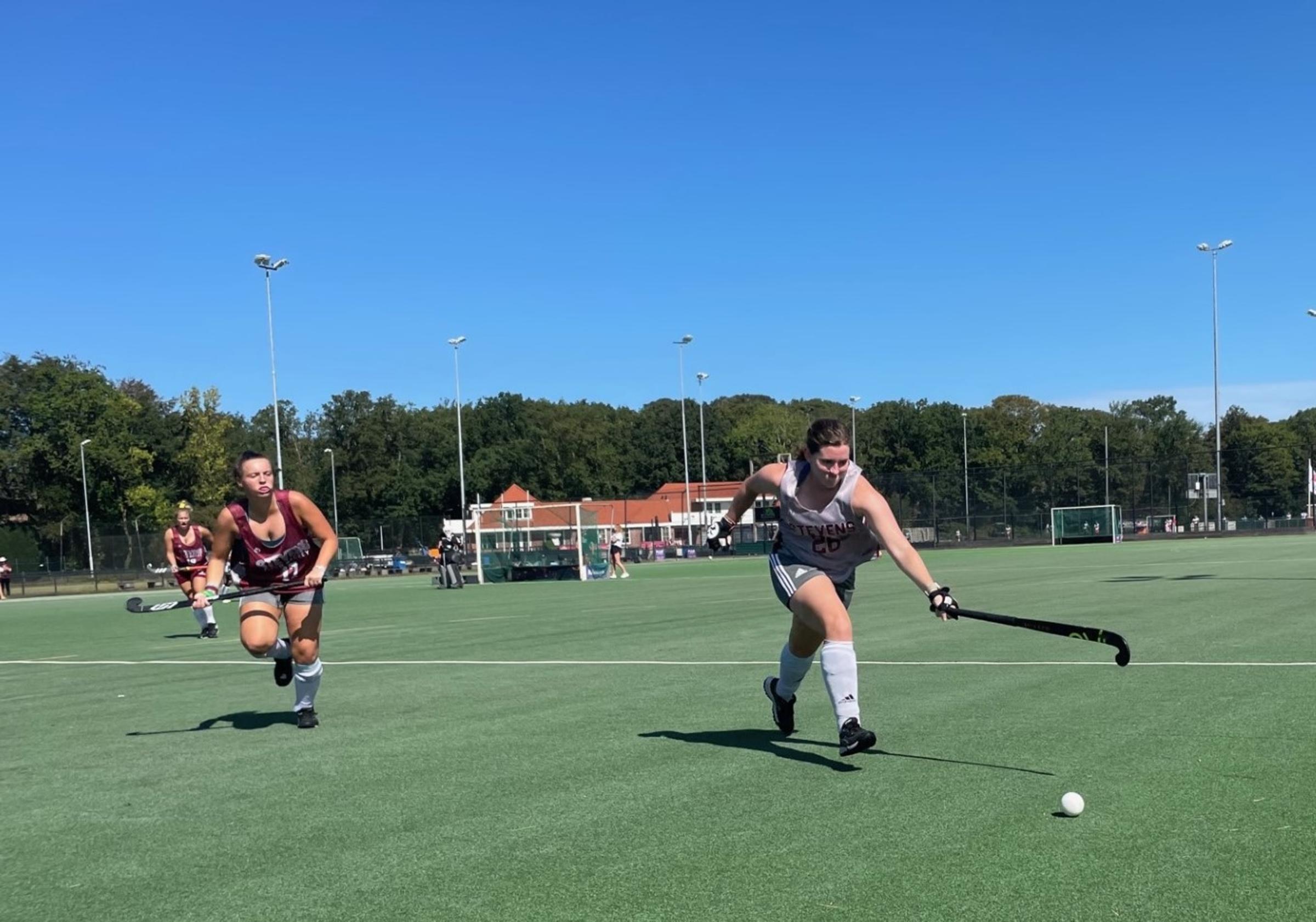 Three field hockey players race up the field