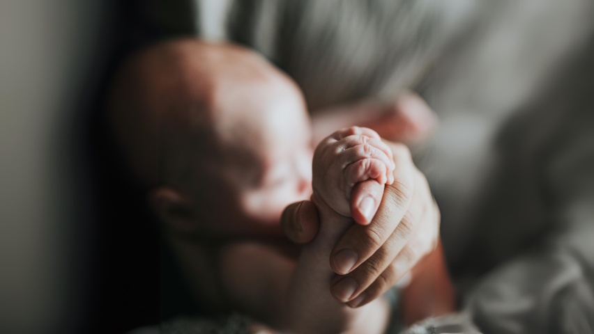 A newborn baby grasping the hand of an adult
