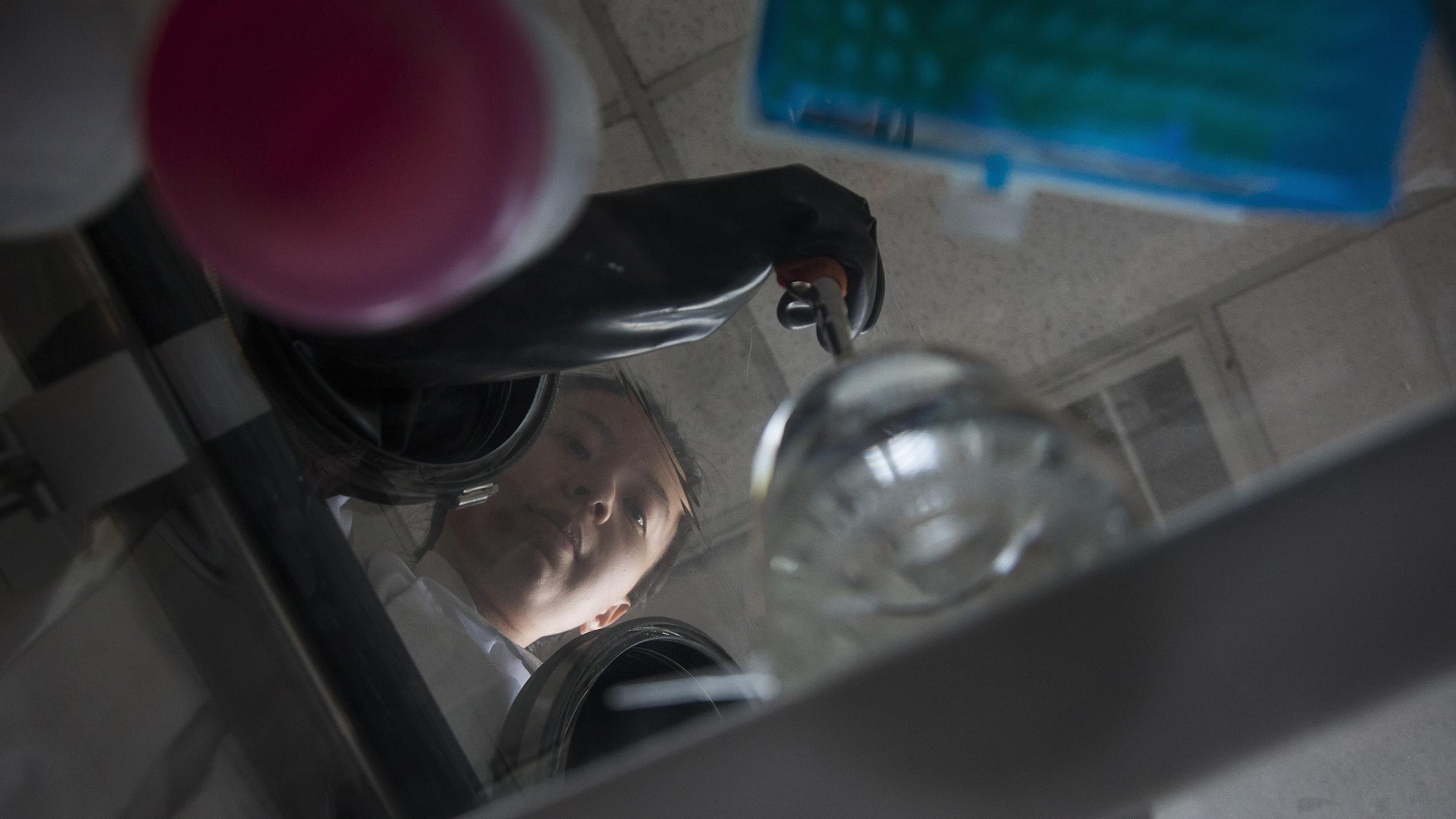 Photo of female student experimenting in lab, from the angle of beneath a glass table of her looking down