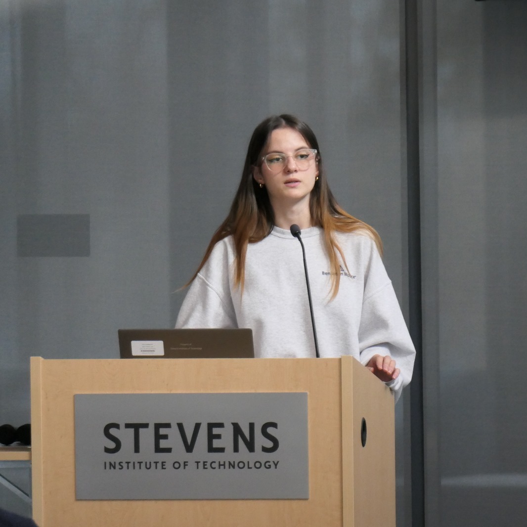 Bertila Bruka standing at a presentation podium speaking to a group of people.