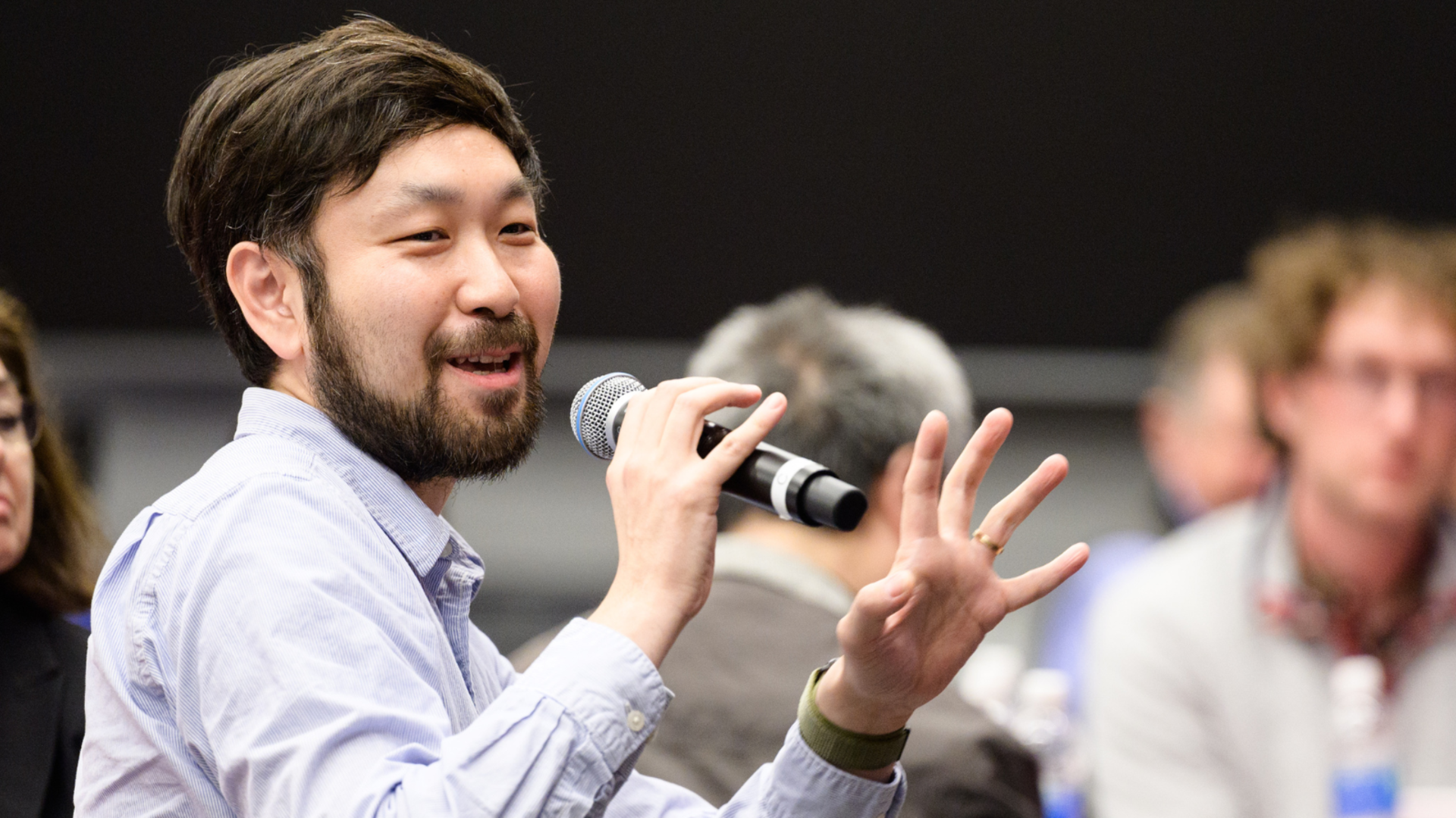 A photograph of Long Wang speaking into a microphone.