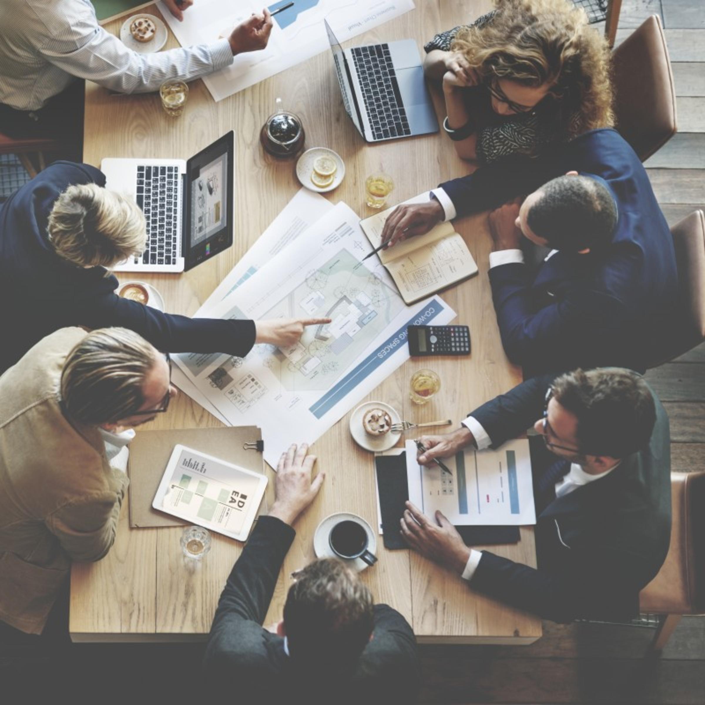 Stock of Individuals working at table with laptops and plans