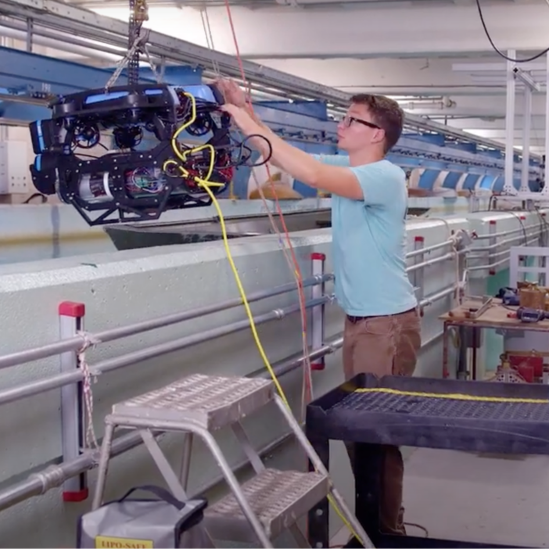 A student moves an underwater robot into a testing water tank while a professor and another student assist.