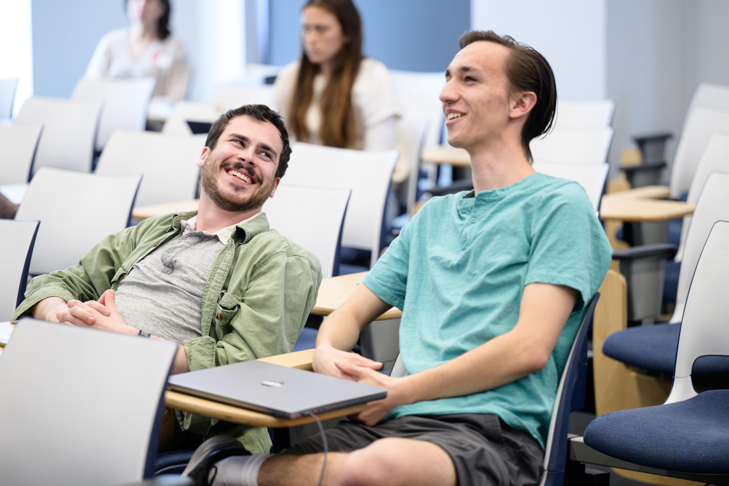 Two male students sitting in desk chairs having a conversation.