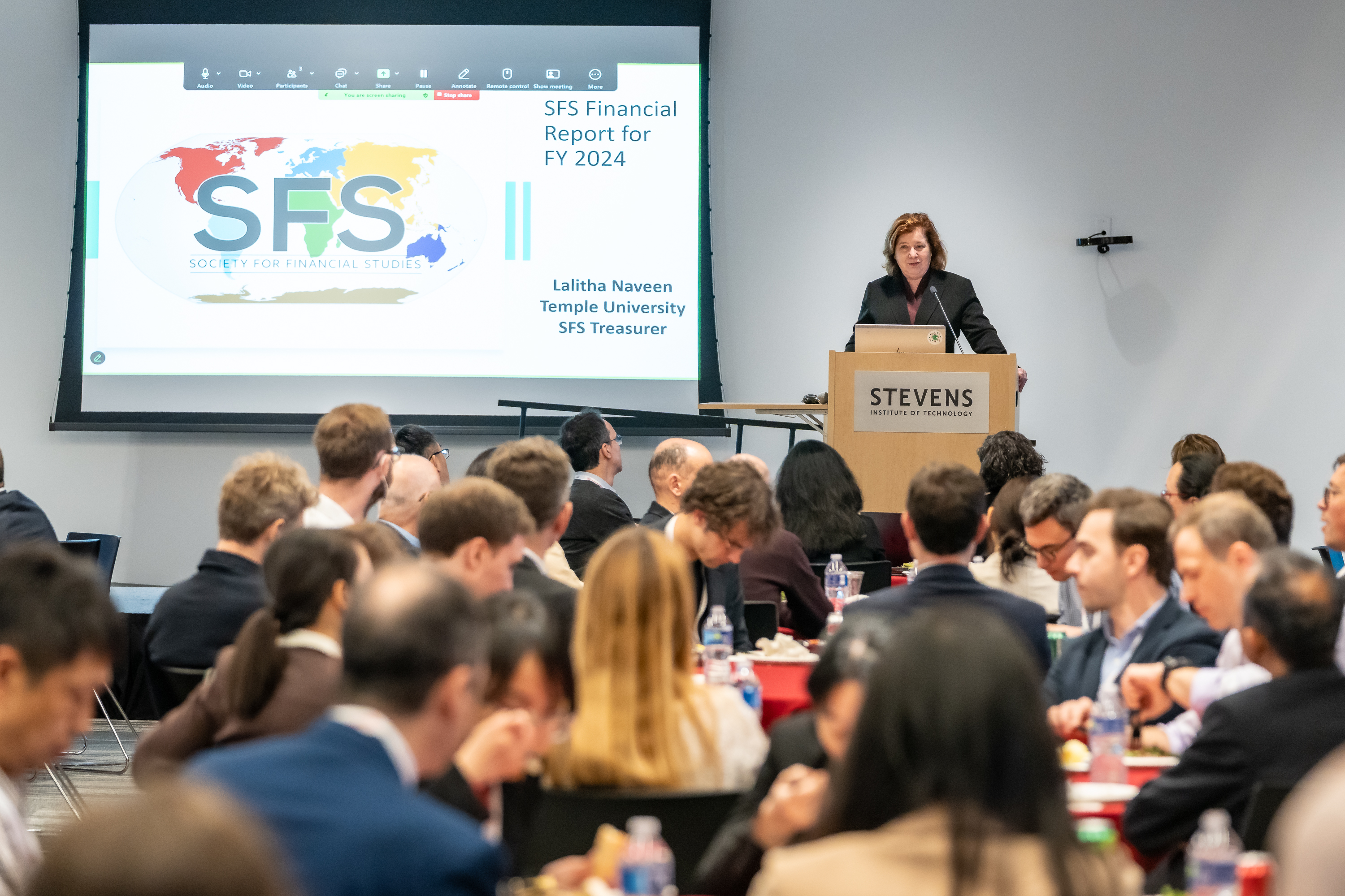 A woman stands on stage behind a podium in front of a slide with the SFS Cavalcade logo.