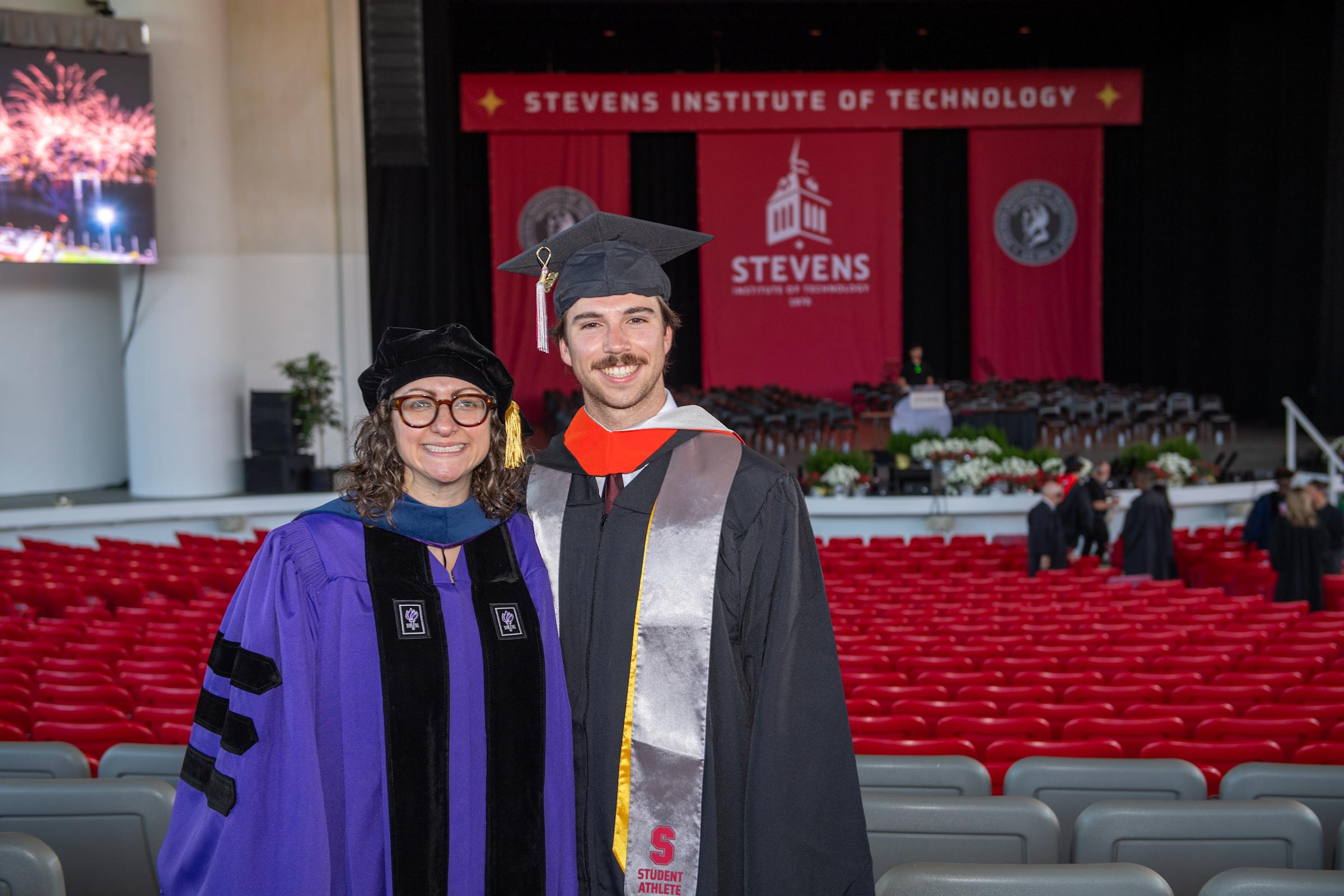 A woman and man in Commencement regalia pose together