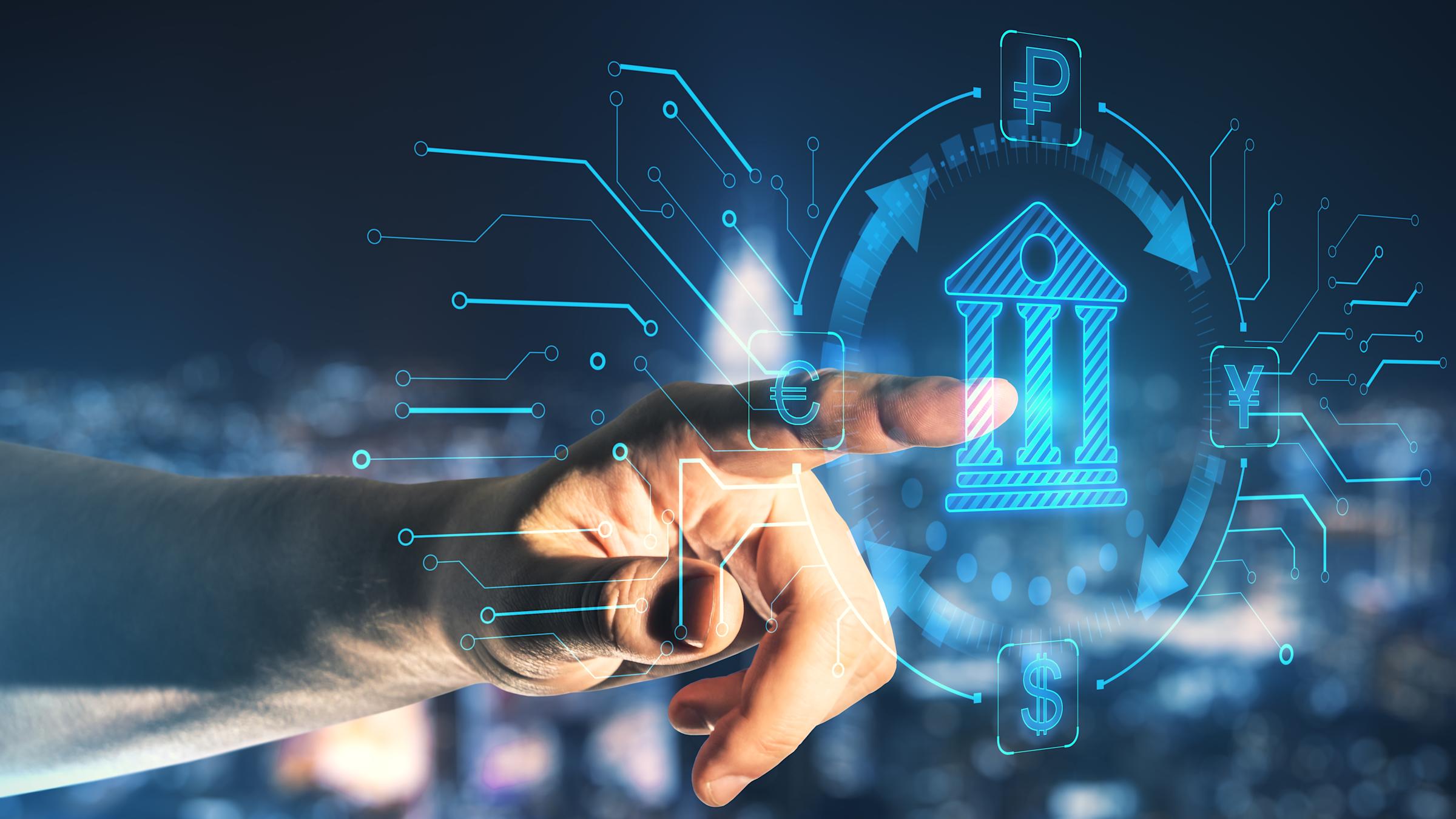 Hand pointing at a glowing blue hologram of a bank building, circled by exchange arrows linking euro, ruble, yen and dollar symbols, with circuit lines branching out against a blurred city skyline at night.