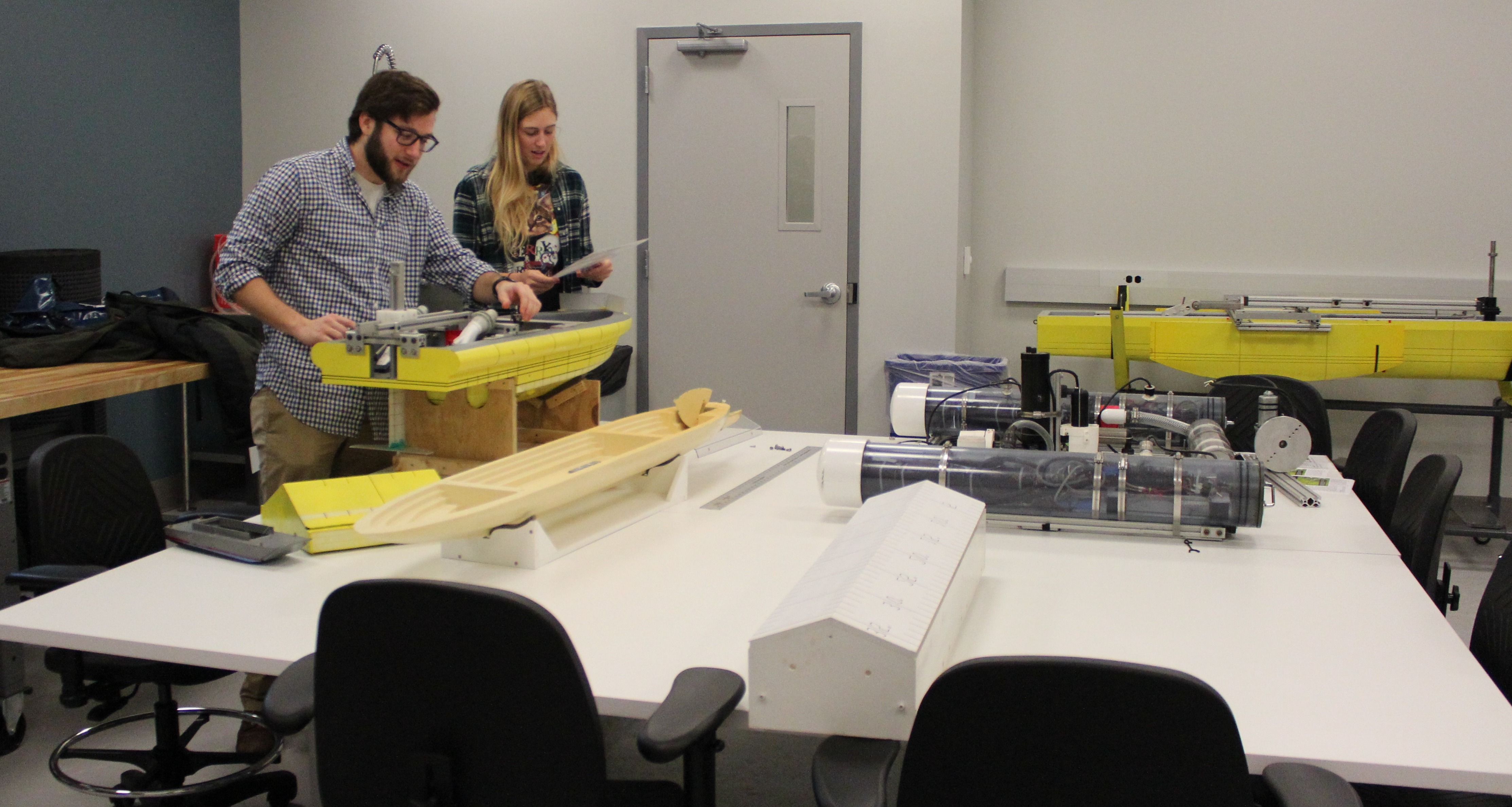 A male and female student in a class room building a boat