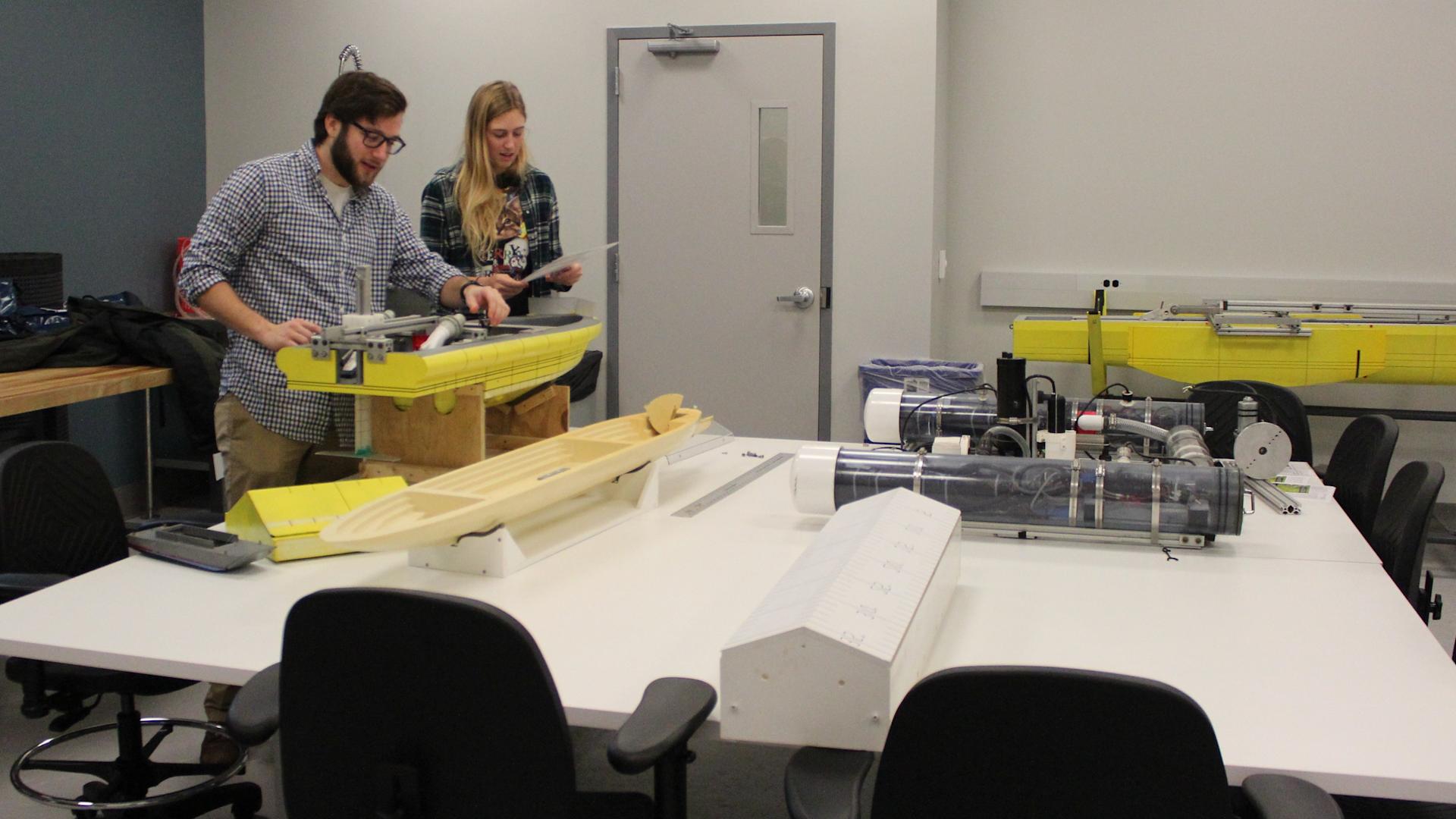 A male and female student in a class room building a boat