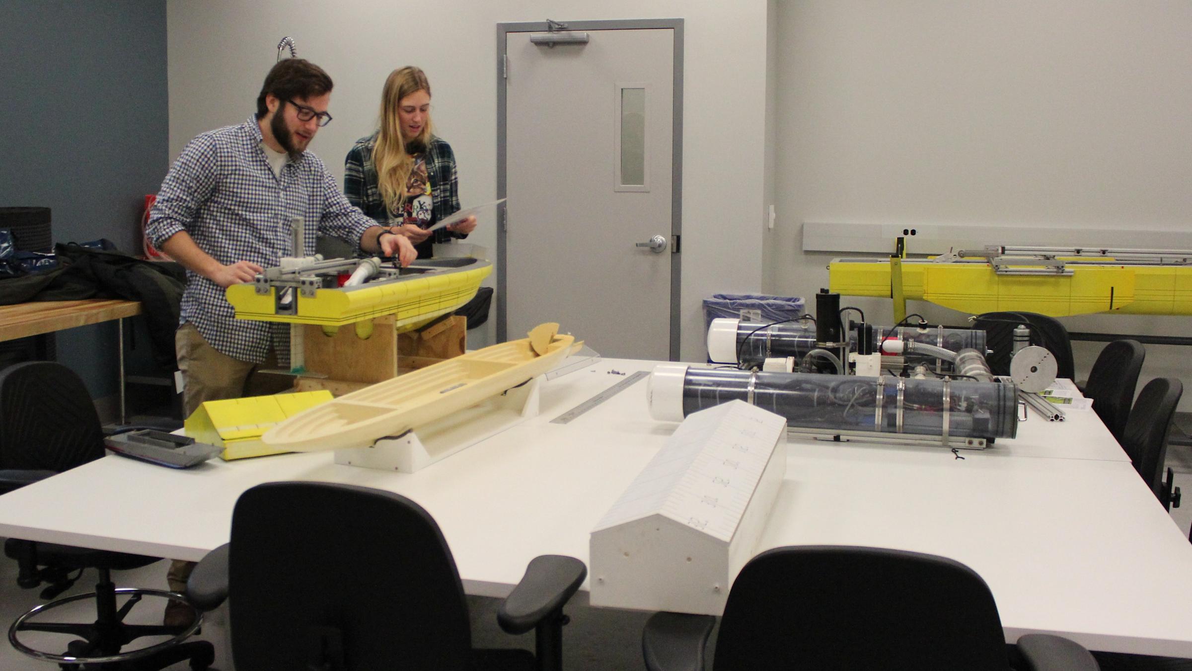A male and female student in a class room building a boat