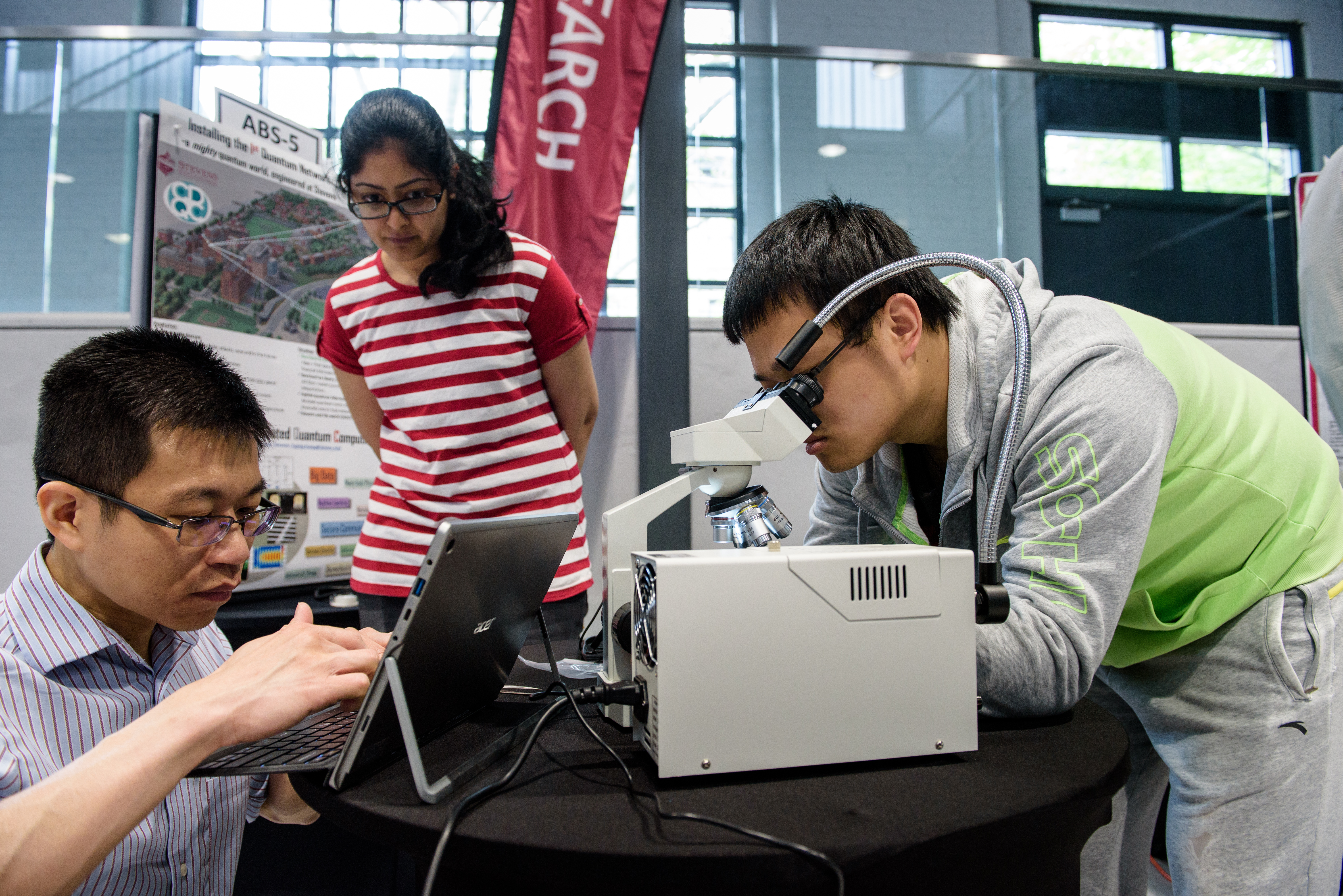Three students examine equipment during a project display of a quantum computing network.