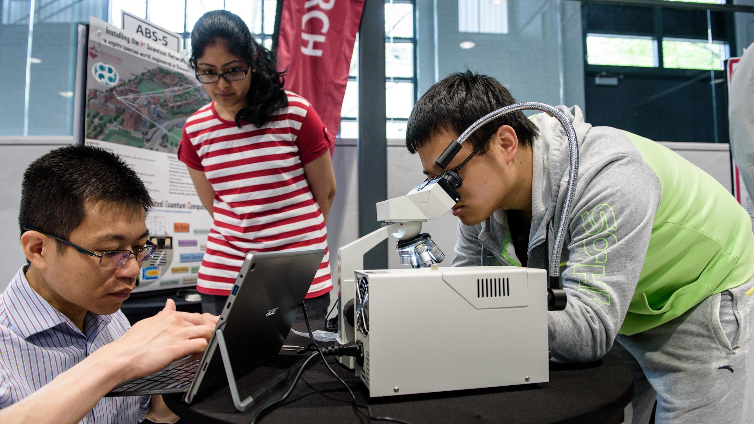 Three students examine equipment during a project display of a quantum computing network.